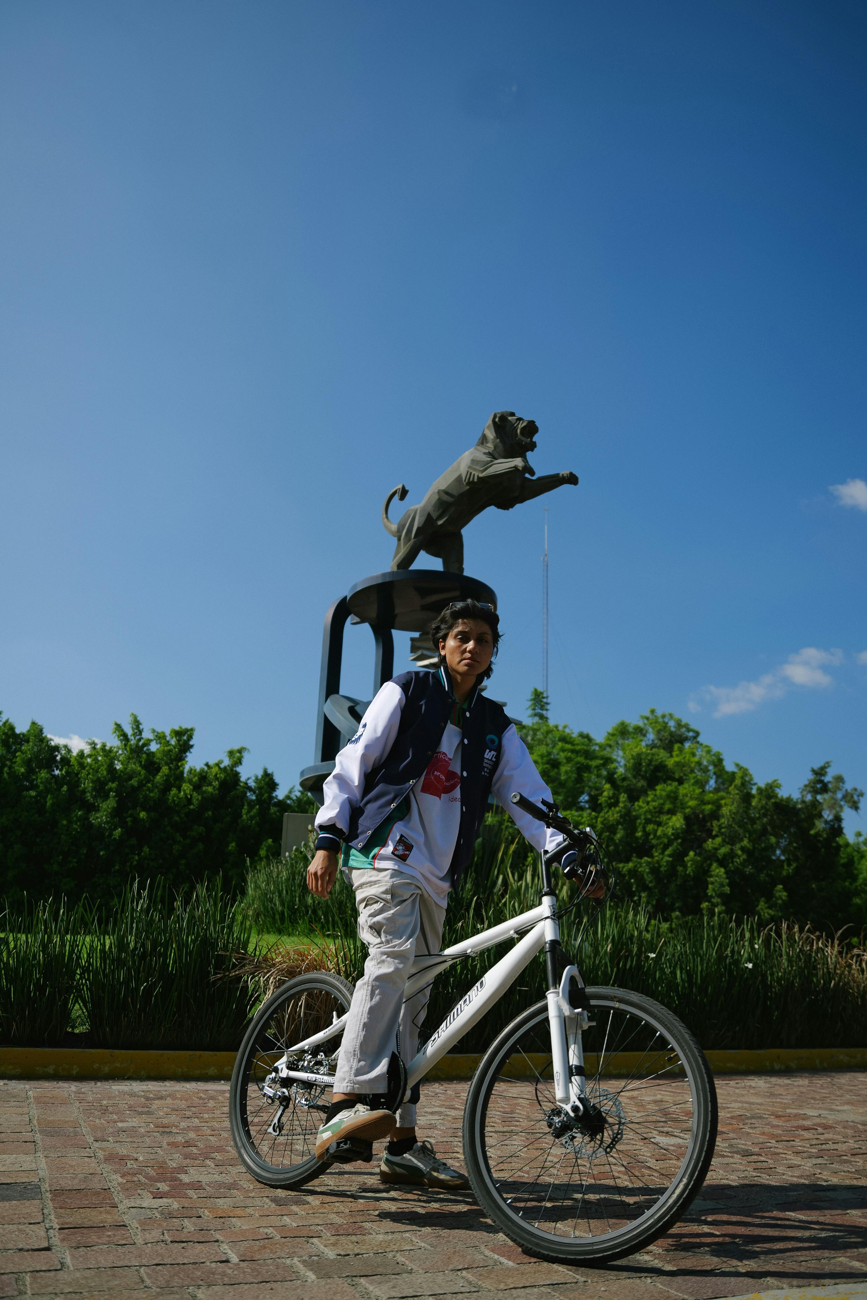 Young man cycling near León Puma Monument in León, Mexico under clear blue sky.