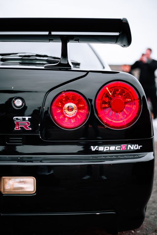 Free Detailed view of red tail lights on a black sports car, highlighting the GTR emblem and V-Spec II Nür badge. Stock Photo