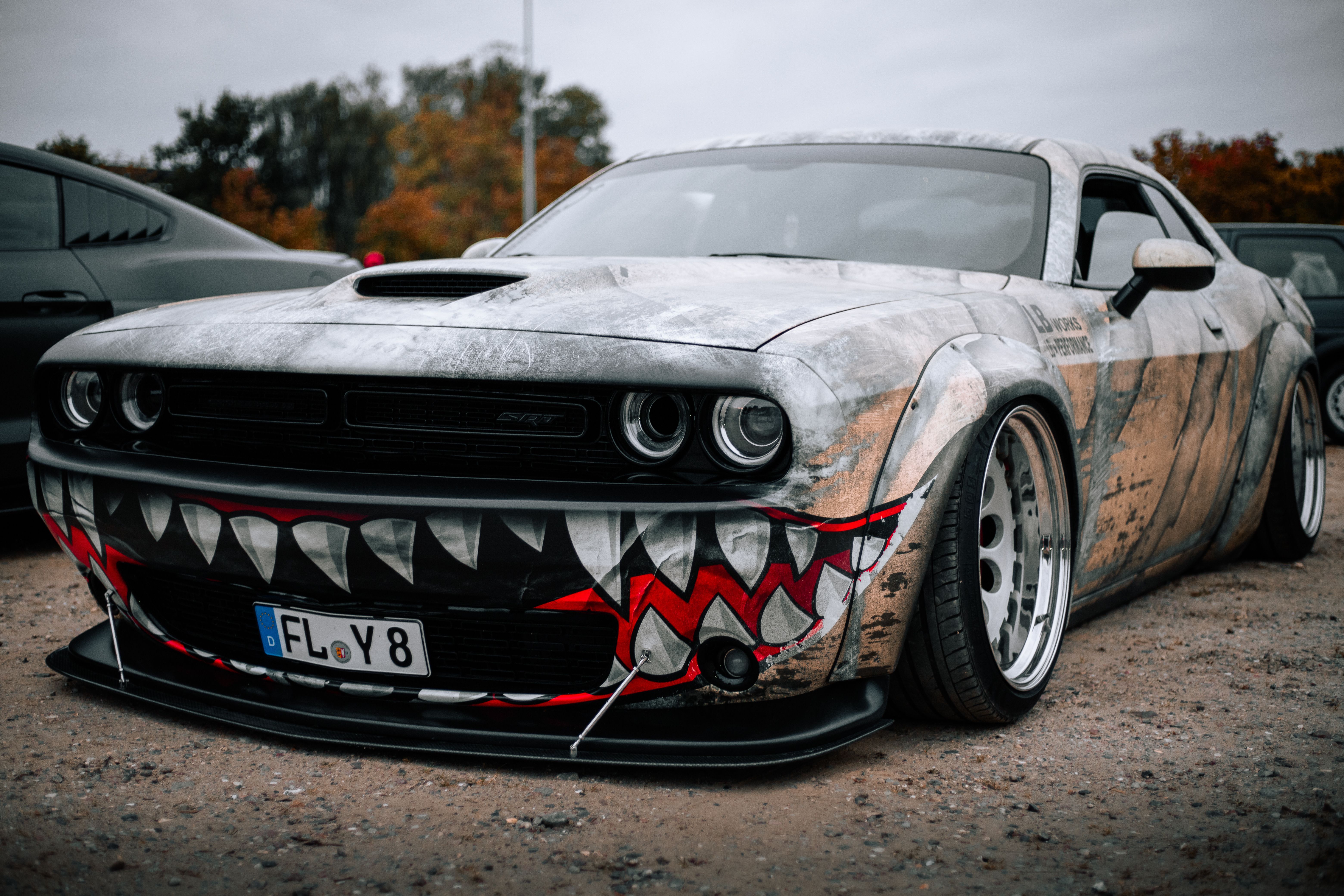 Custom car with striking shark airbrush design set in an autumn outdoor parking area.