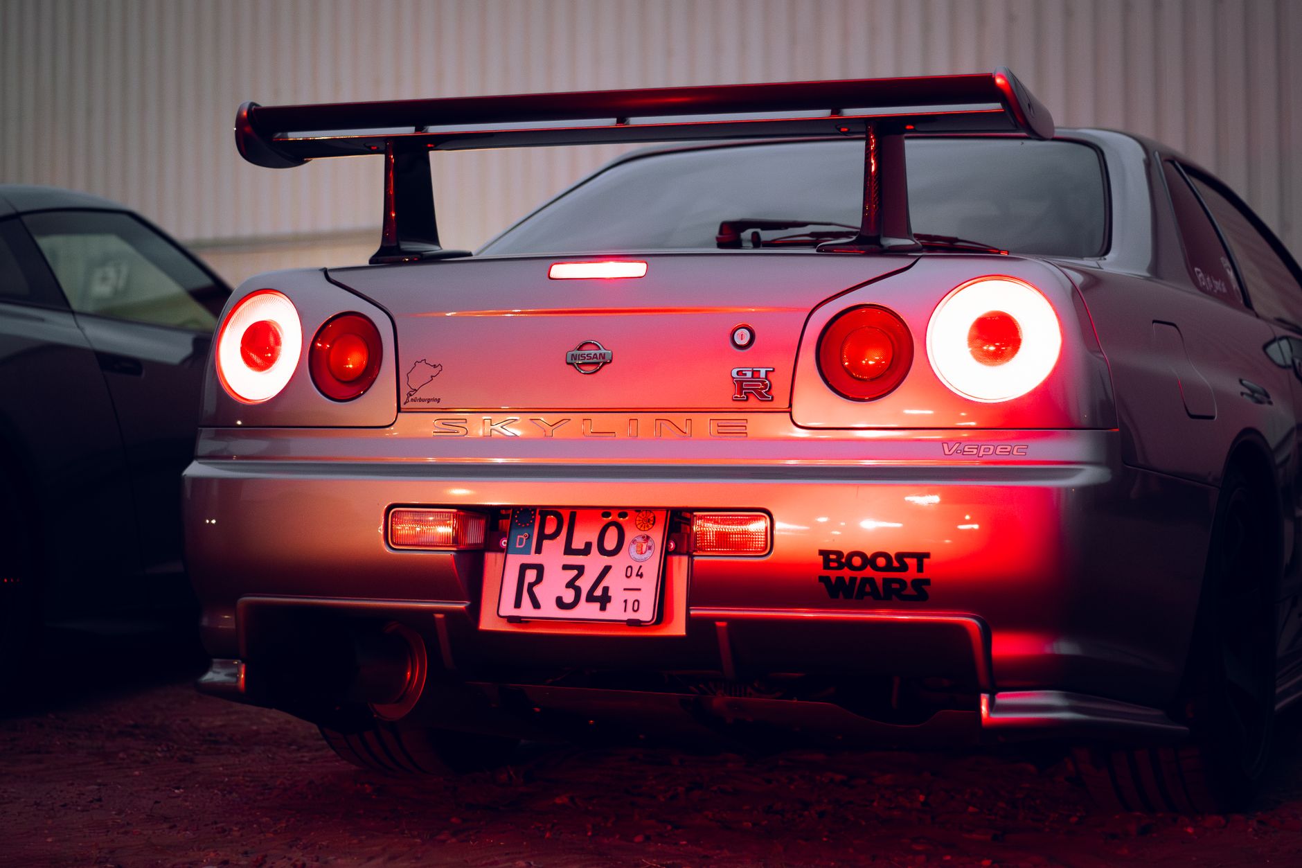 Classic sports car with distinctive spoiler and glowing tail lights at night, parked in an urban setting.