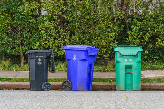 Photo by Robert So Black, blue, and green recycling bins on the street curb, ready for collection.