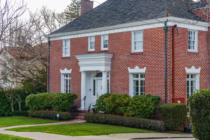 Red brick home with white trim and an established front garden