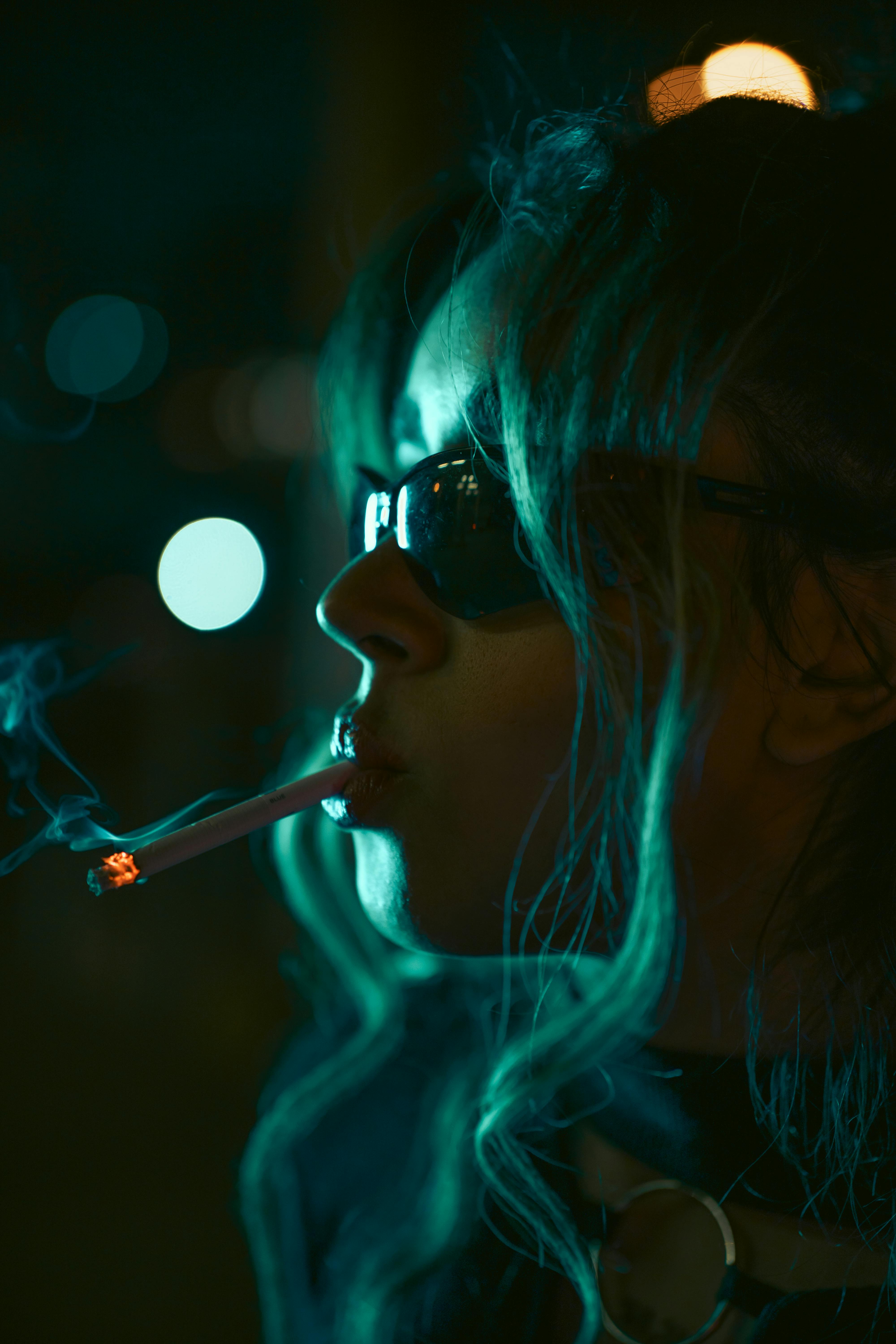 grátis Um misterioso retrato noturno retratando uma mulher fumando um cigarro, projetando sombras dramáticas. Foto profissional