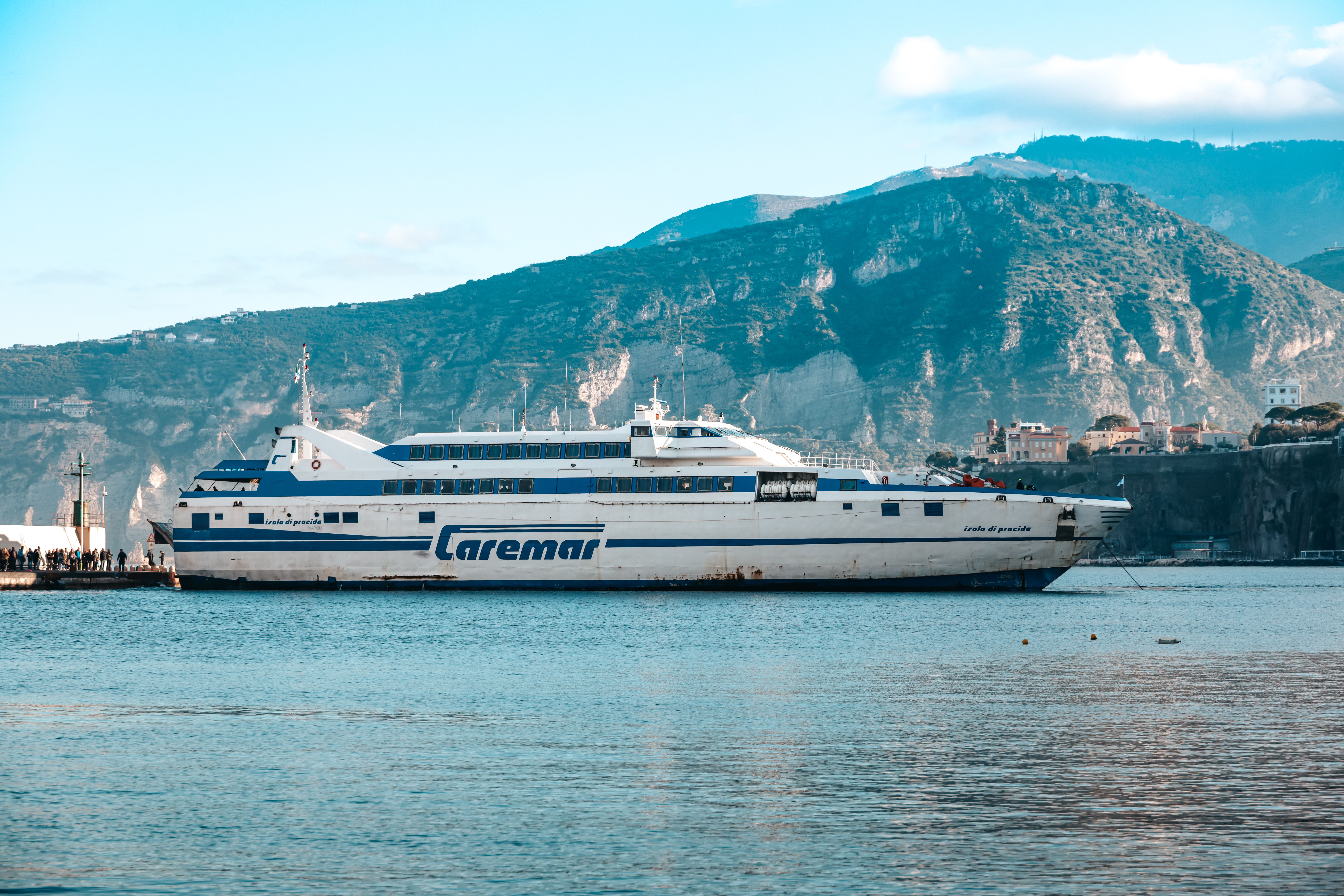 Caremar ferry docked by a mountainous Italian coastline under a bright blue sky