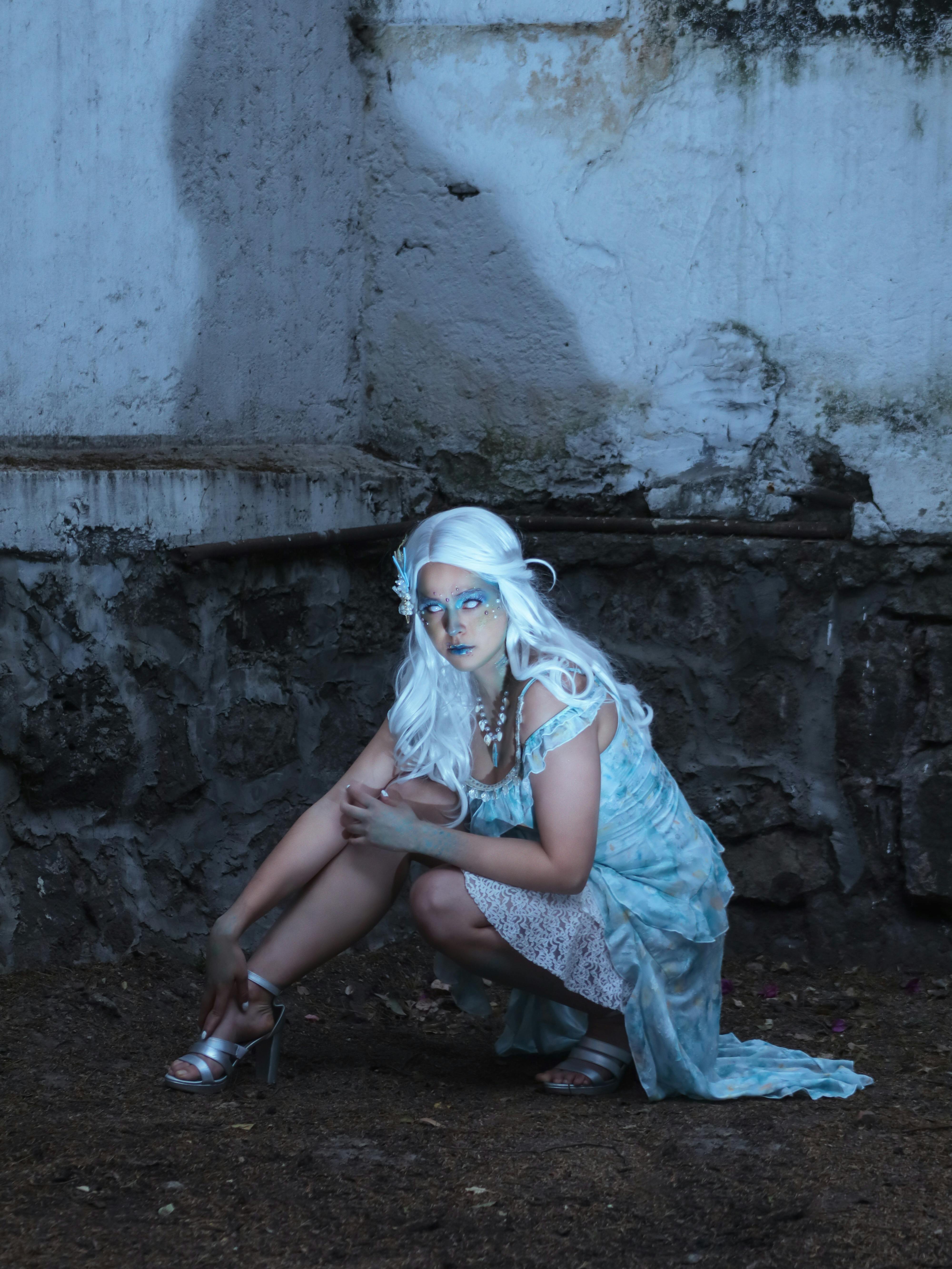 Miễn phí Một người phụ nữ thanh tú với mái tóc bạc đang ngồi xổm trong một khung cảnh u ám, tối tăm. Ảnh lưu trữ