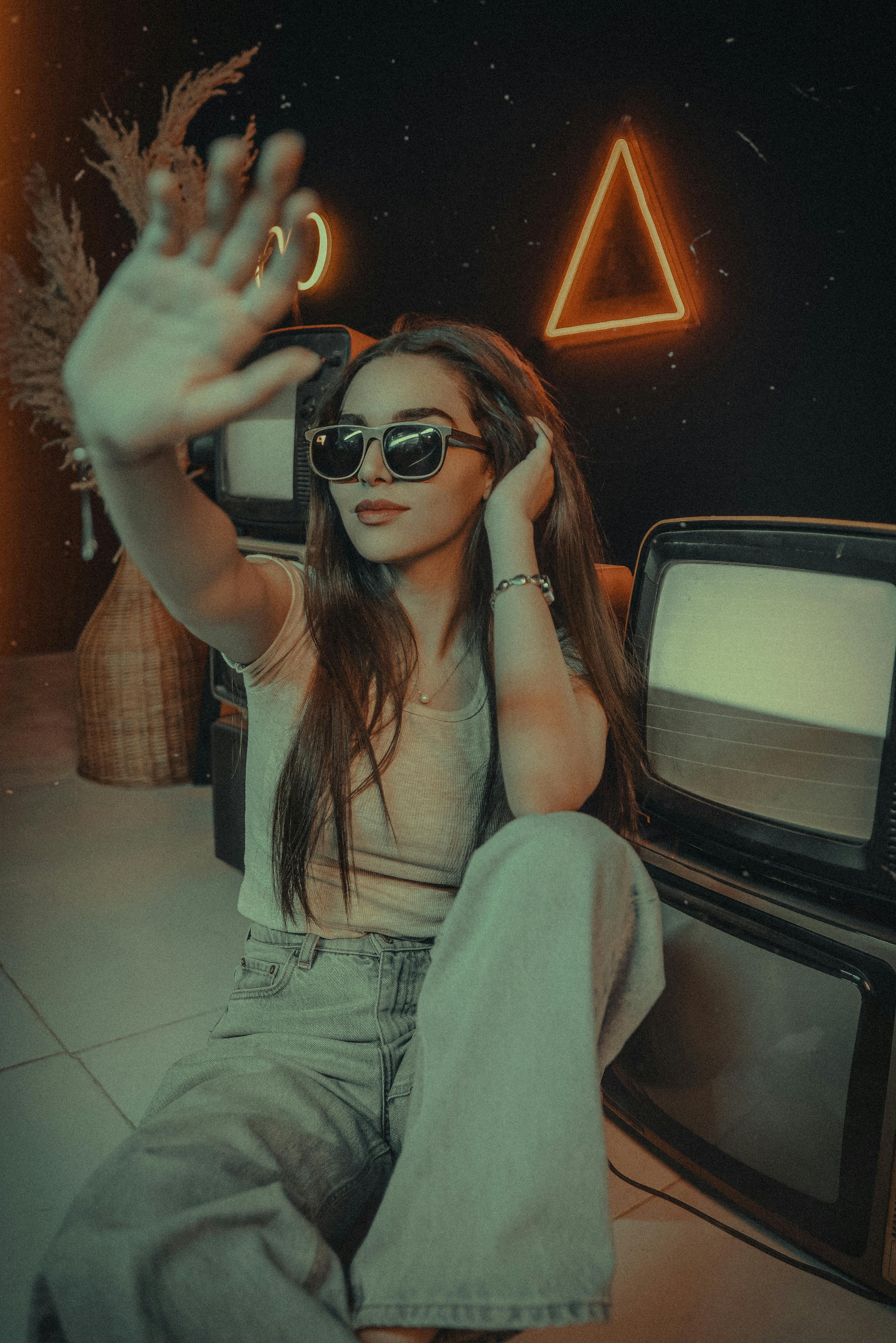 Δωρεάν Κομψή γυναίκα με γυαλιά ηλίου ποζάρει με νέον φώτα και vintage τηλεοράσεις για μια μοντέρνα αισθητική. Φωτογραφία από στοκ φωτογραφιών