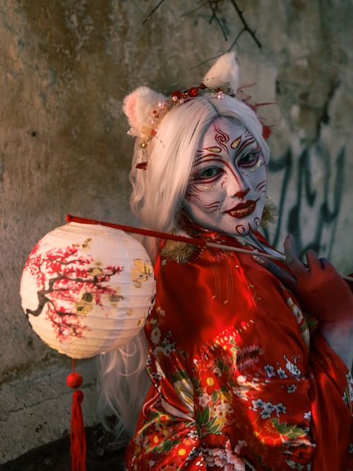 Free A performer in a red kimono with a lantern and elaborate face paint set in a mysterious setting. Stock Photo
