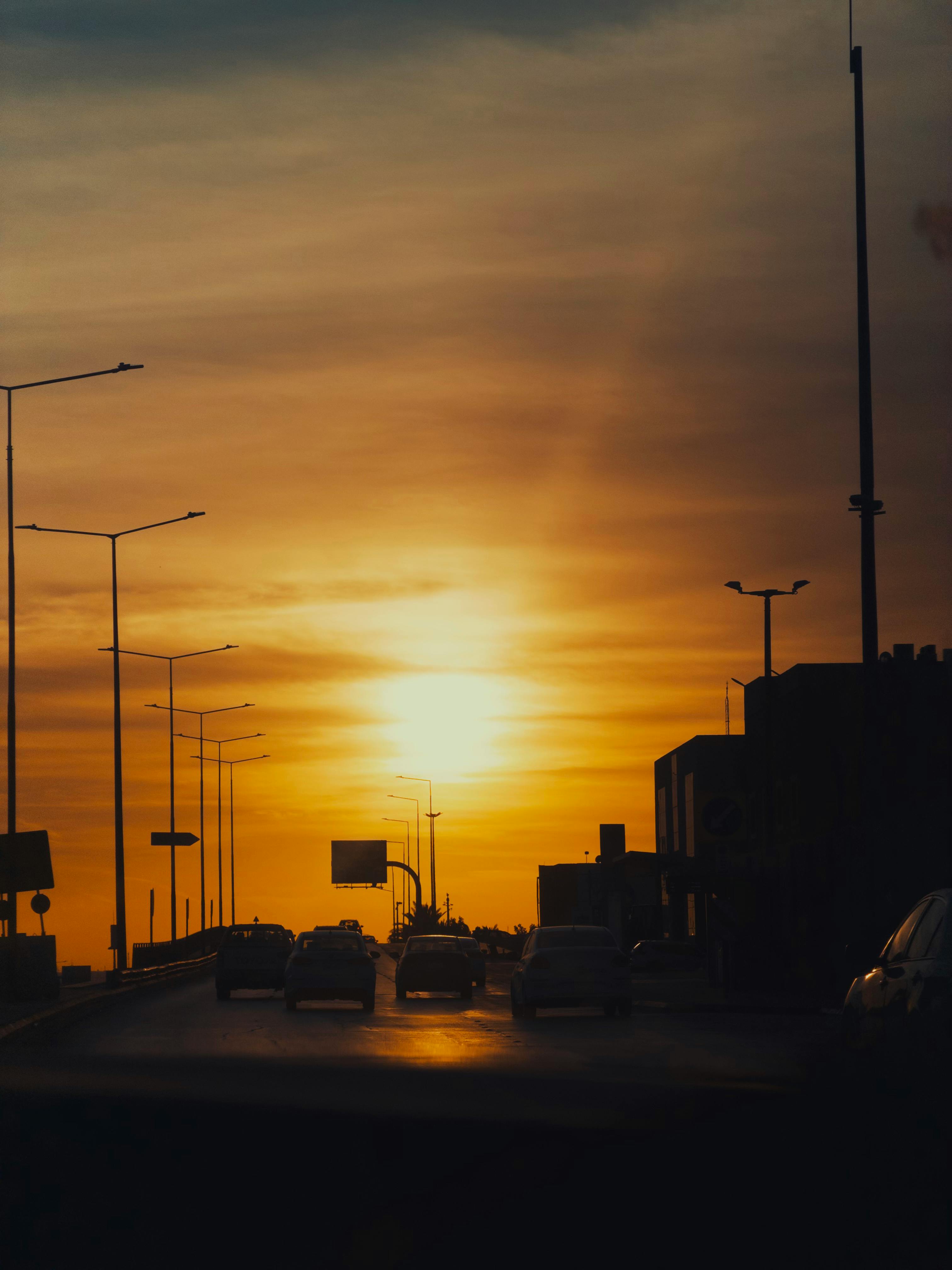 Kostnadsfria Siluett av fordon mot en livlig solnedgång på en trafikerad stadsmotorväg, som fångar en dramatisk och varm atmosfär. Stock foto