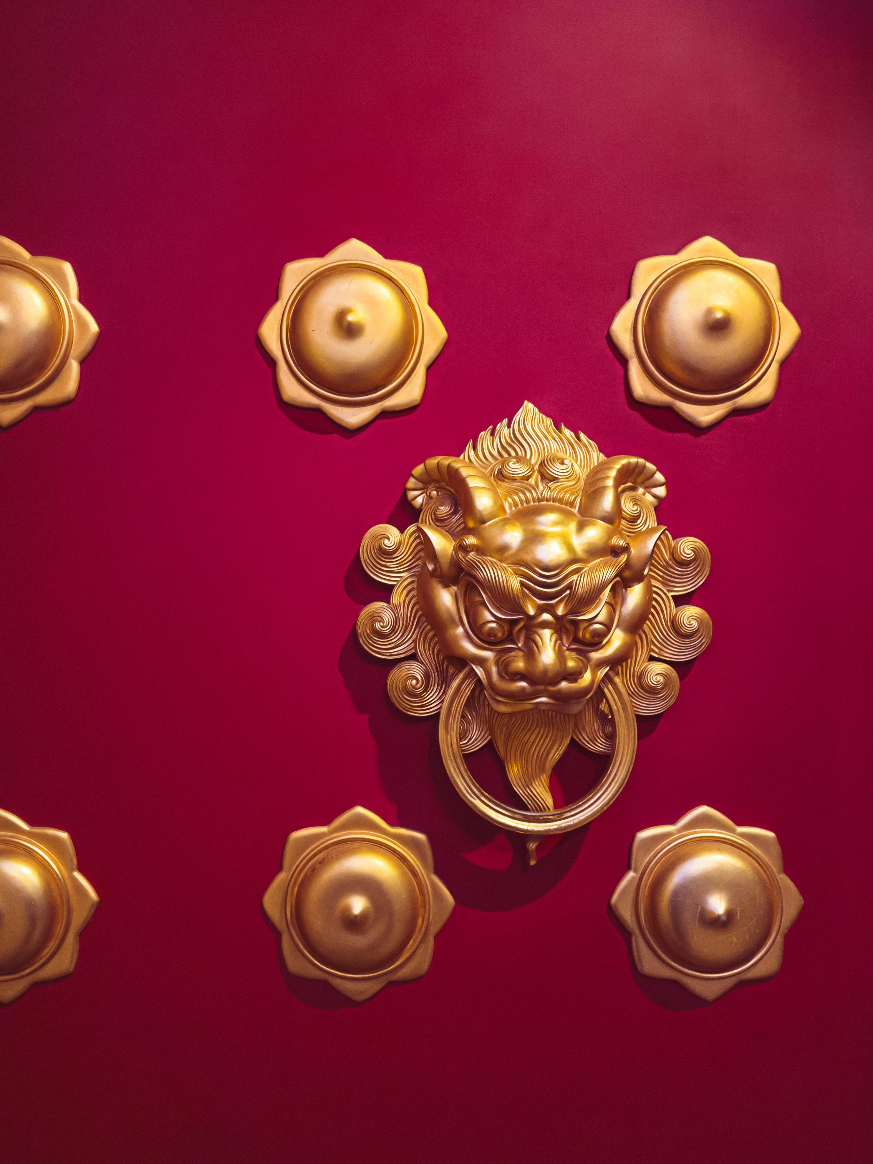 Ilmainen Koristeellinen kultainen leijona-ovenkolkutin eloisanpunaisessa ovessa, joka on perinteisen kiinalaisen muotoilun ruumiillistuma. Kuvapankkikuva