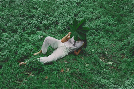 A woman relaxing outdoors on lush green foliage, holding a large leaf over her face.