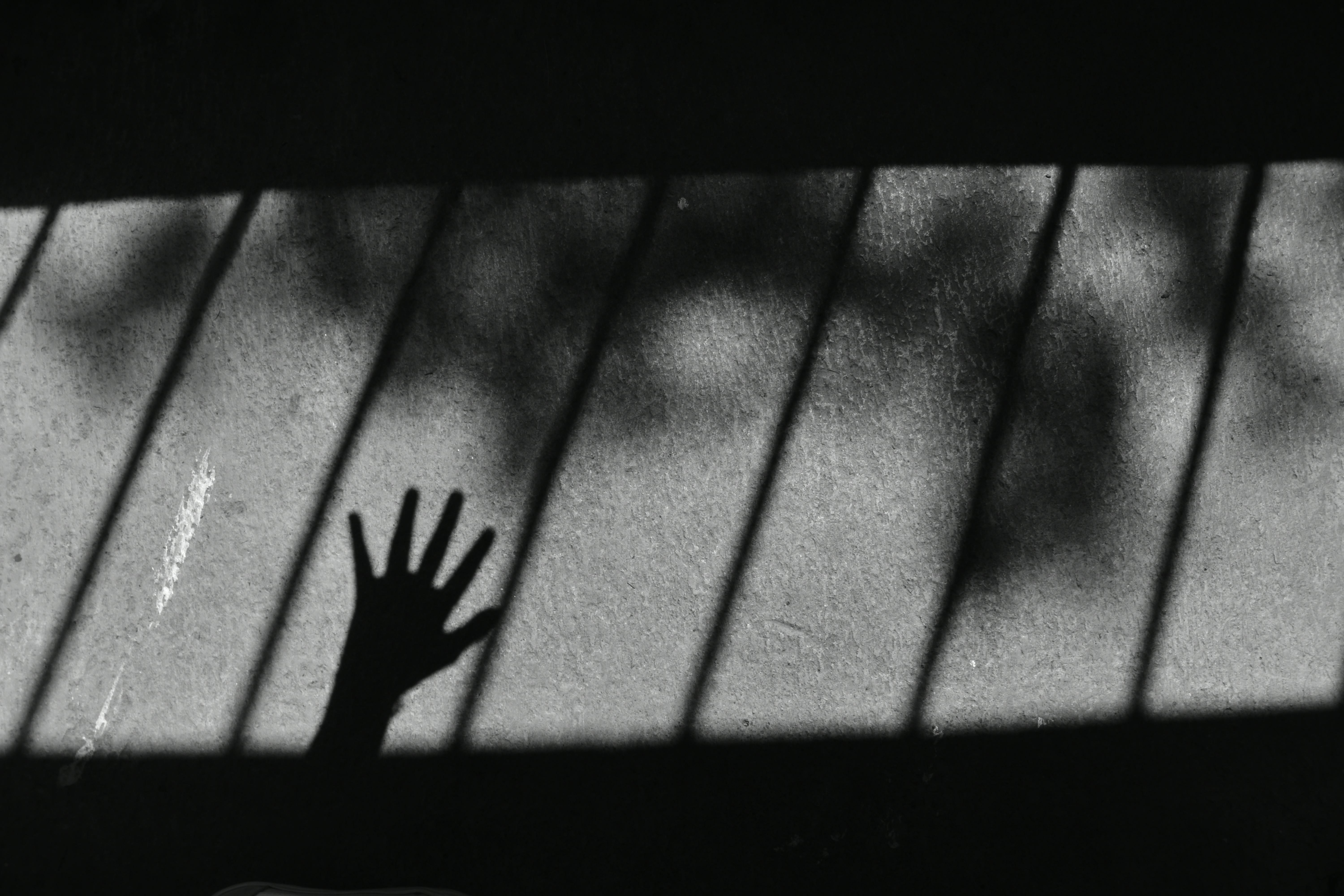 Gratis Fotografía artística en blanco y negro de la sombra de una mano proyectada sobre una superficie de hormigón con sombras rayadas. Foto de stock
