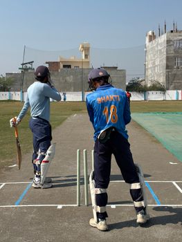 Two cricket players in full gear practicing on a cricket pitch in a sunny outdoor setting.