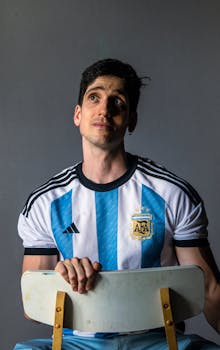 Portrait of a man wearing an Argentina soccer jersey, seated and gazing upwards.