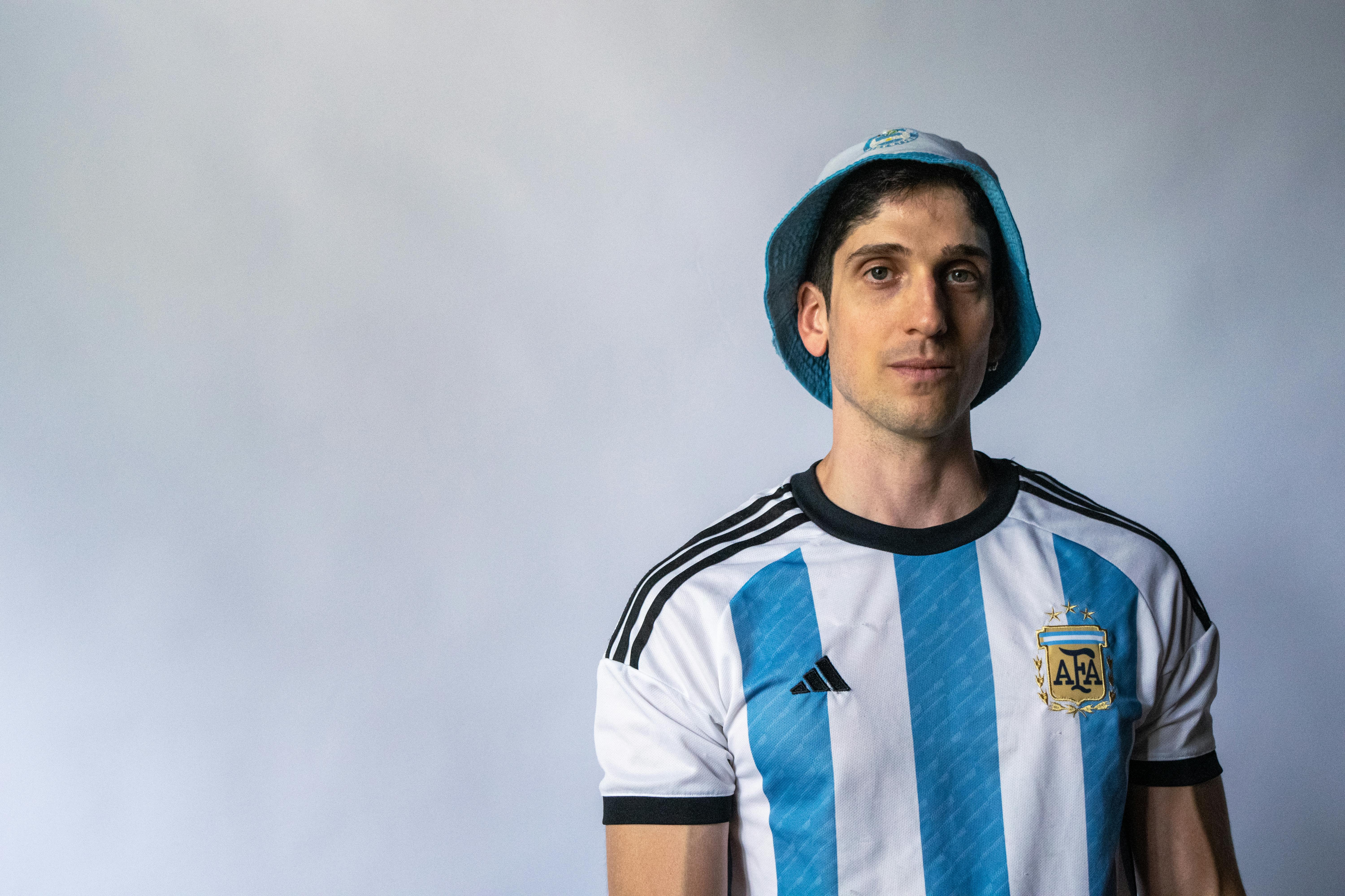 ingyenes Közeli portré egy argentin futballmezt és -sapkát viselő férfiról, egyszerű háttér előtt. Stockfotó