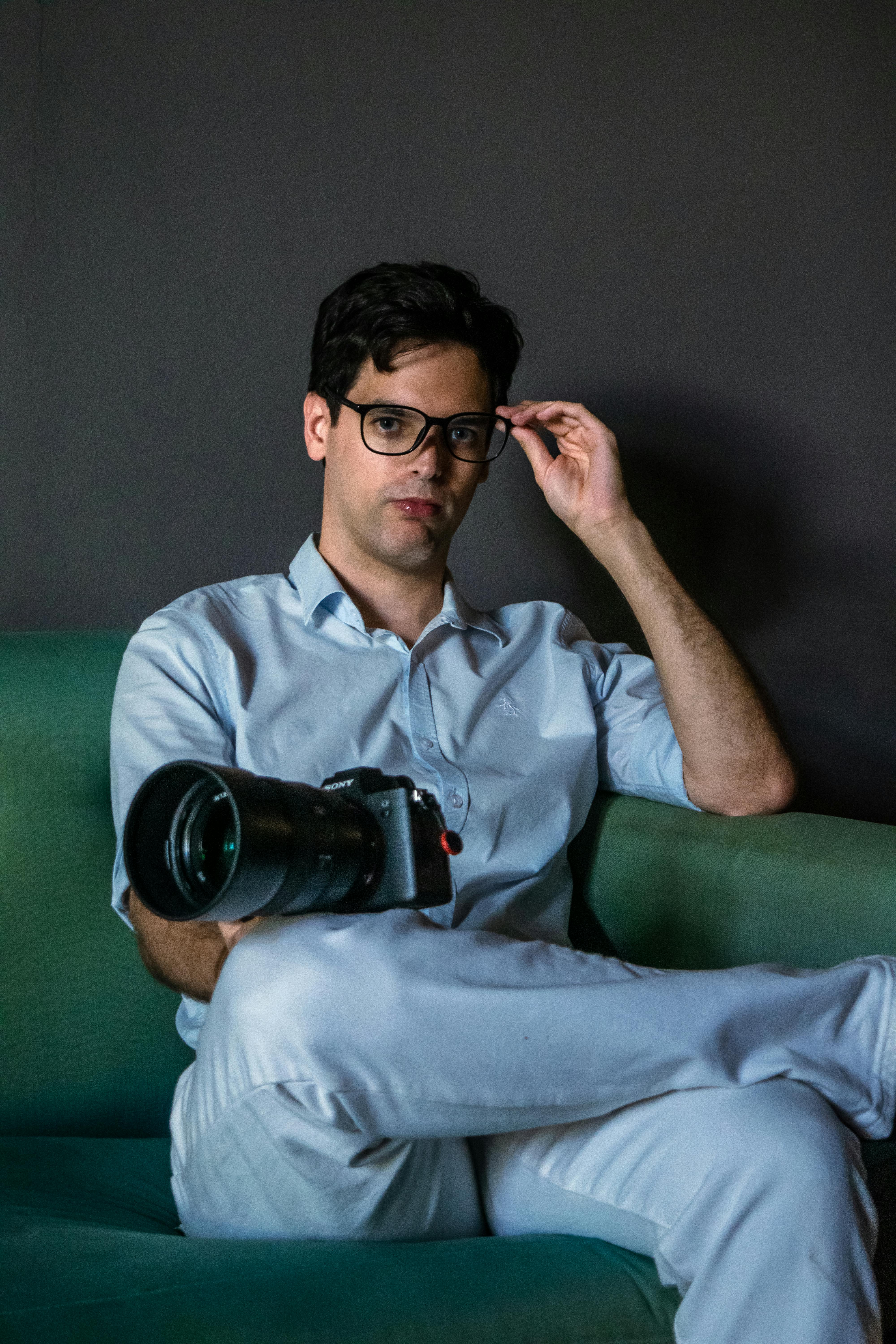 A relaxed professional photographer holding a camera, seated on a green couch indoors.