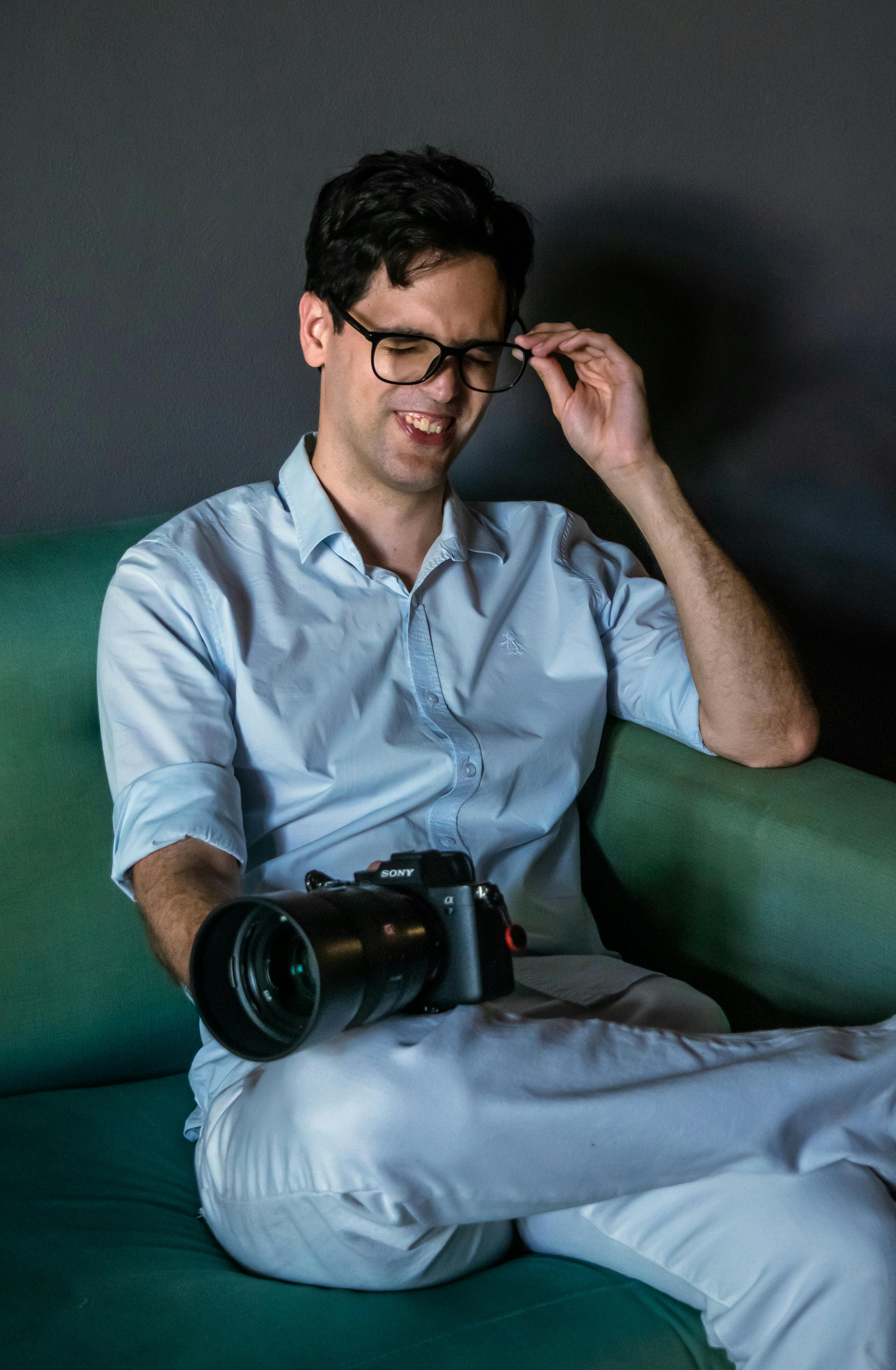 gratis Een lachende man in vrijetijdskleding houdt een camera vast en ontspant zich binnenshuis. Stockfoto