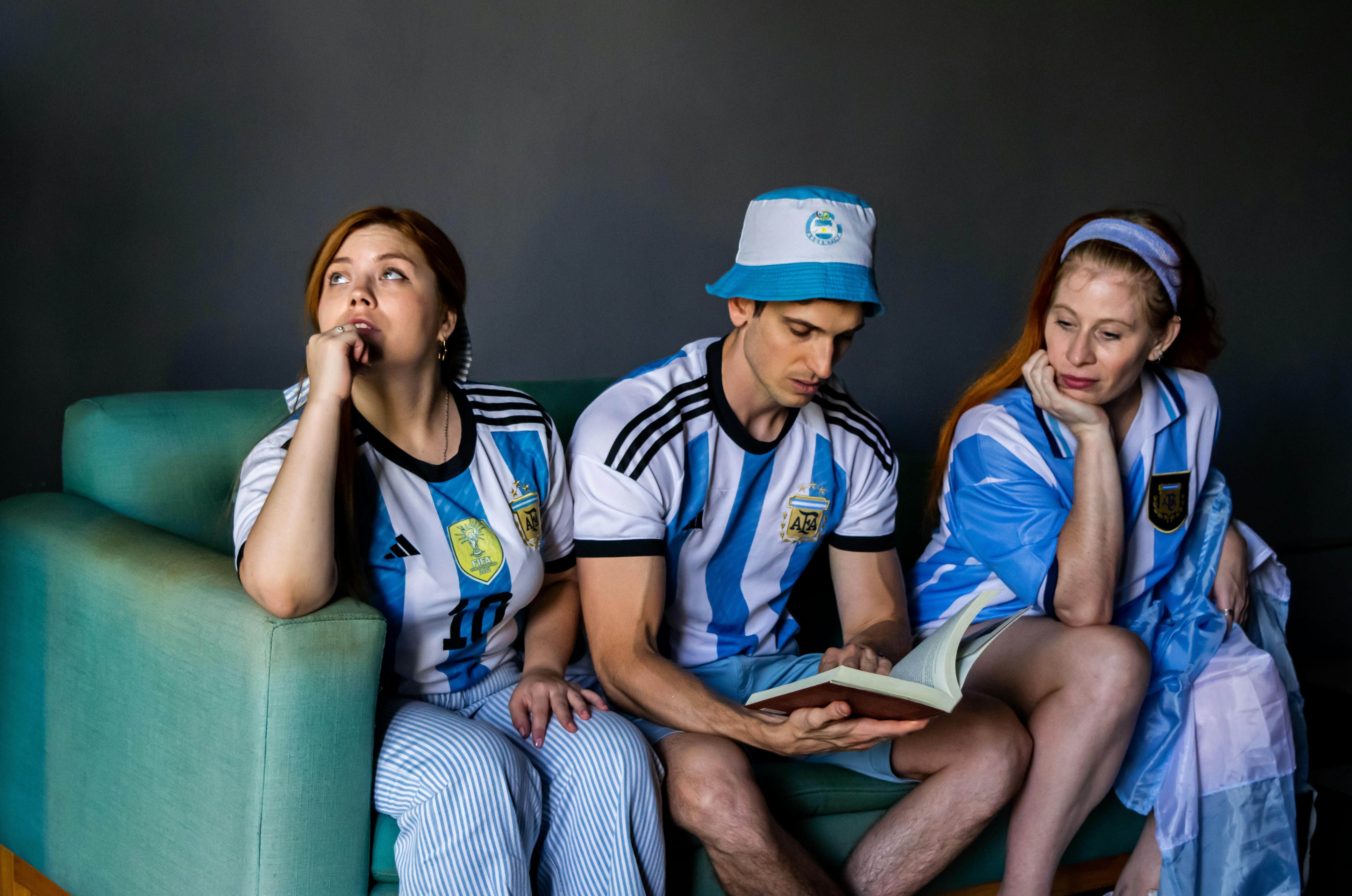 Kostnadsfria Tre vuxna i fotbollströjor kopplar av i en soffa medan de läser en bok inomhus. Stock foto