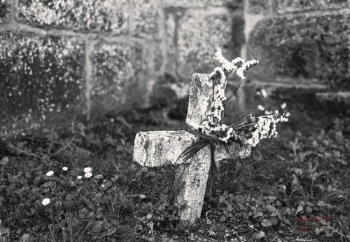 Free A black and white photo of an old stone cross adorned with flowers in a cemetery setting. Stock Photo