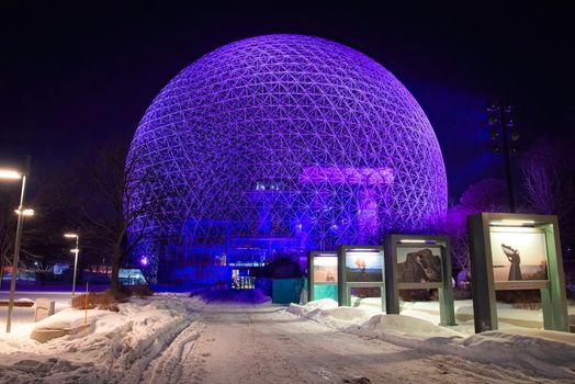Vibrant geodesic dome with purple lighting on a snowy evening, showcasing architectural marvel.