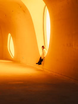 An individual sits in an artistic, warmly lit tunnel with unique architecture.