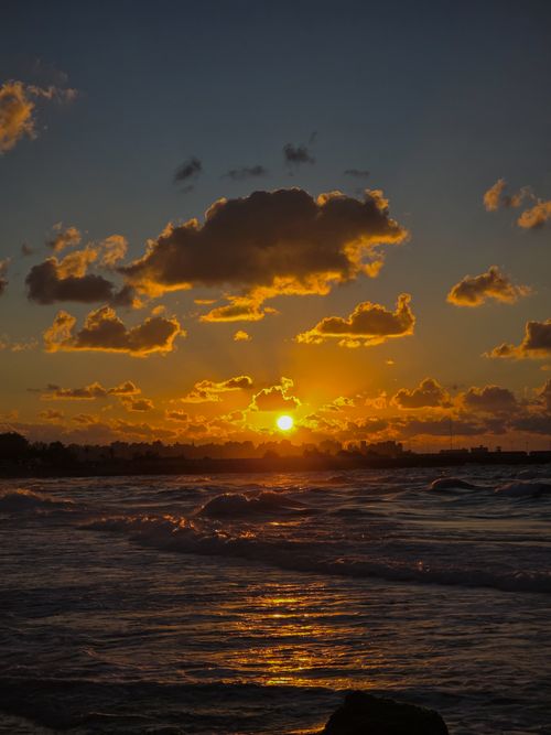 Free Captivating sunset with vivid orange clouds and ocean waves creating a dramatic atmosphere. Stock Photo