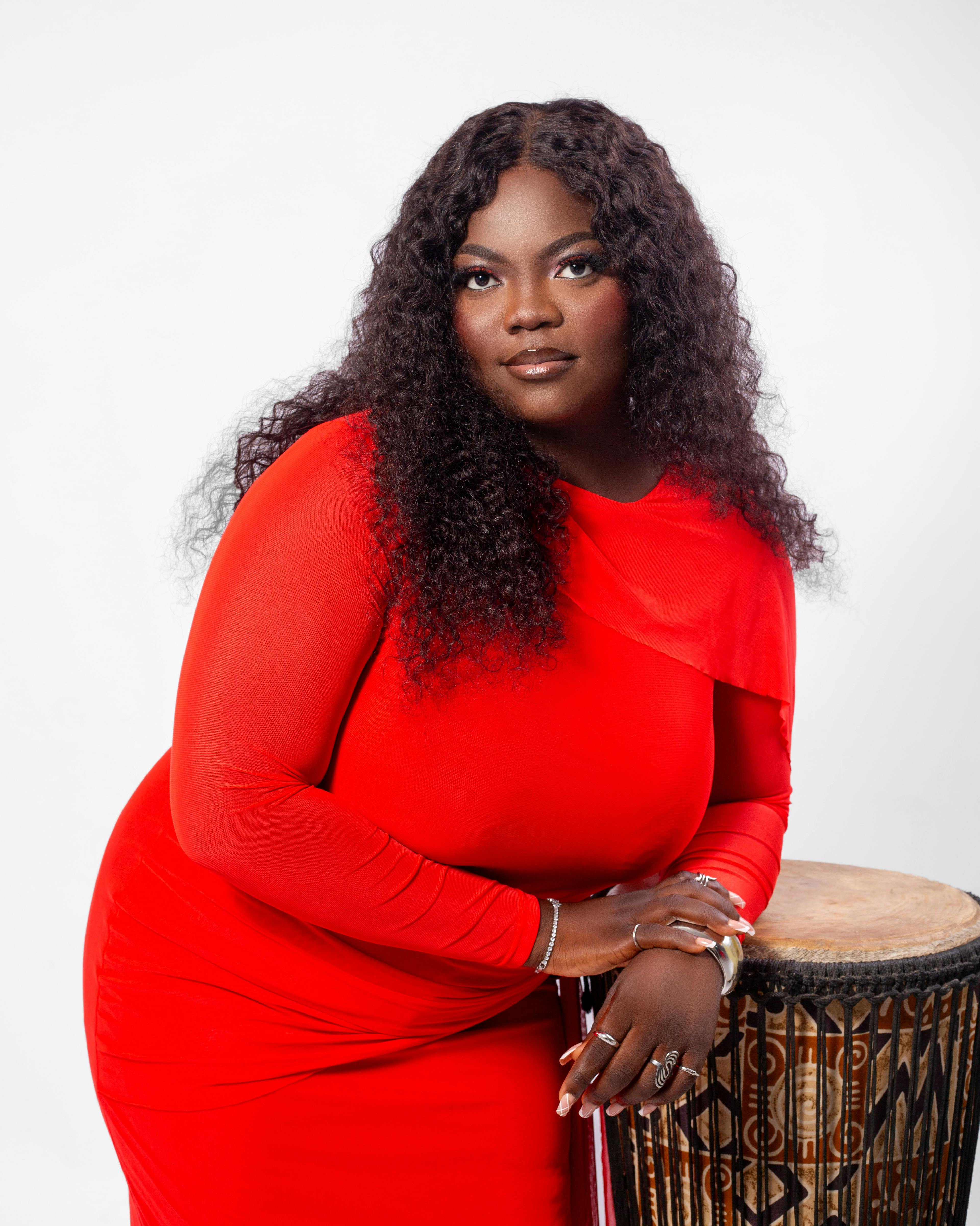 Elegant woman in red dress leaning on African drum, studio shot.