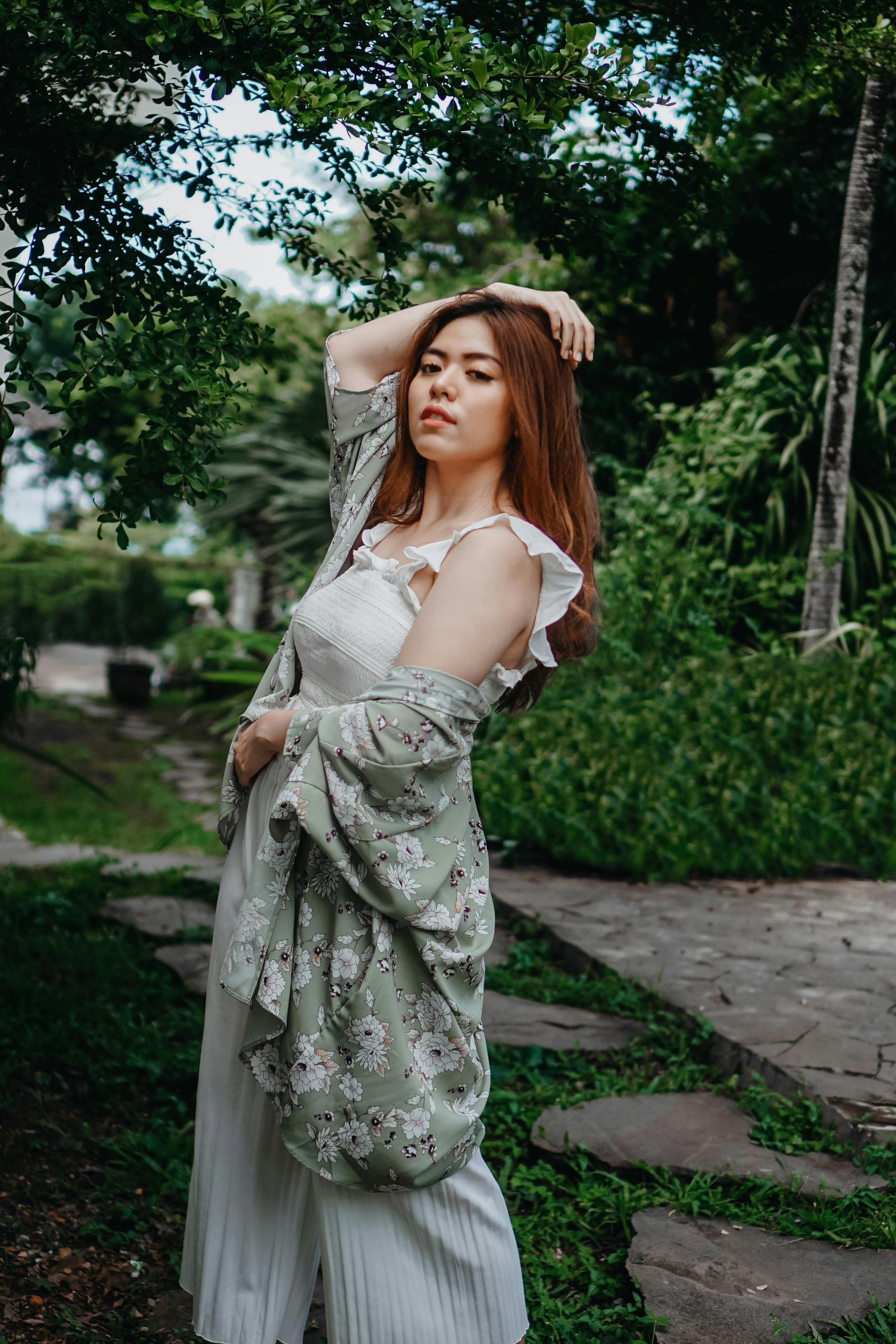 一位身着时尚服装的女士，在郁郁葱葱的户外环境中自信摆姿，尽显优雅气质