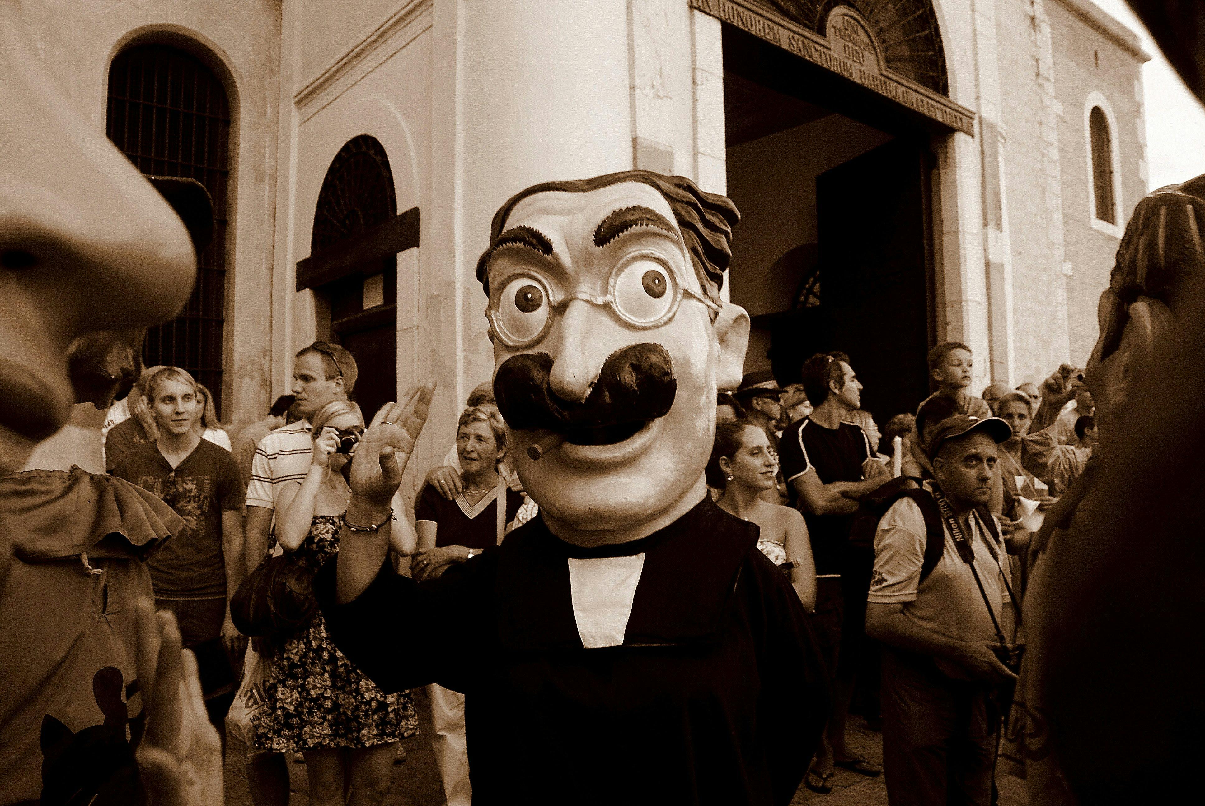 Free Festival scene with a person in a giant mask, surrounded by a crowd in sepia tone. Stock Photo