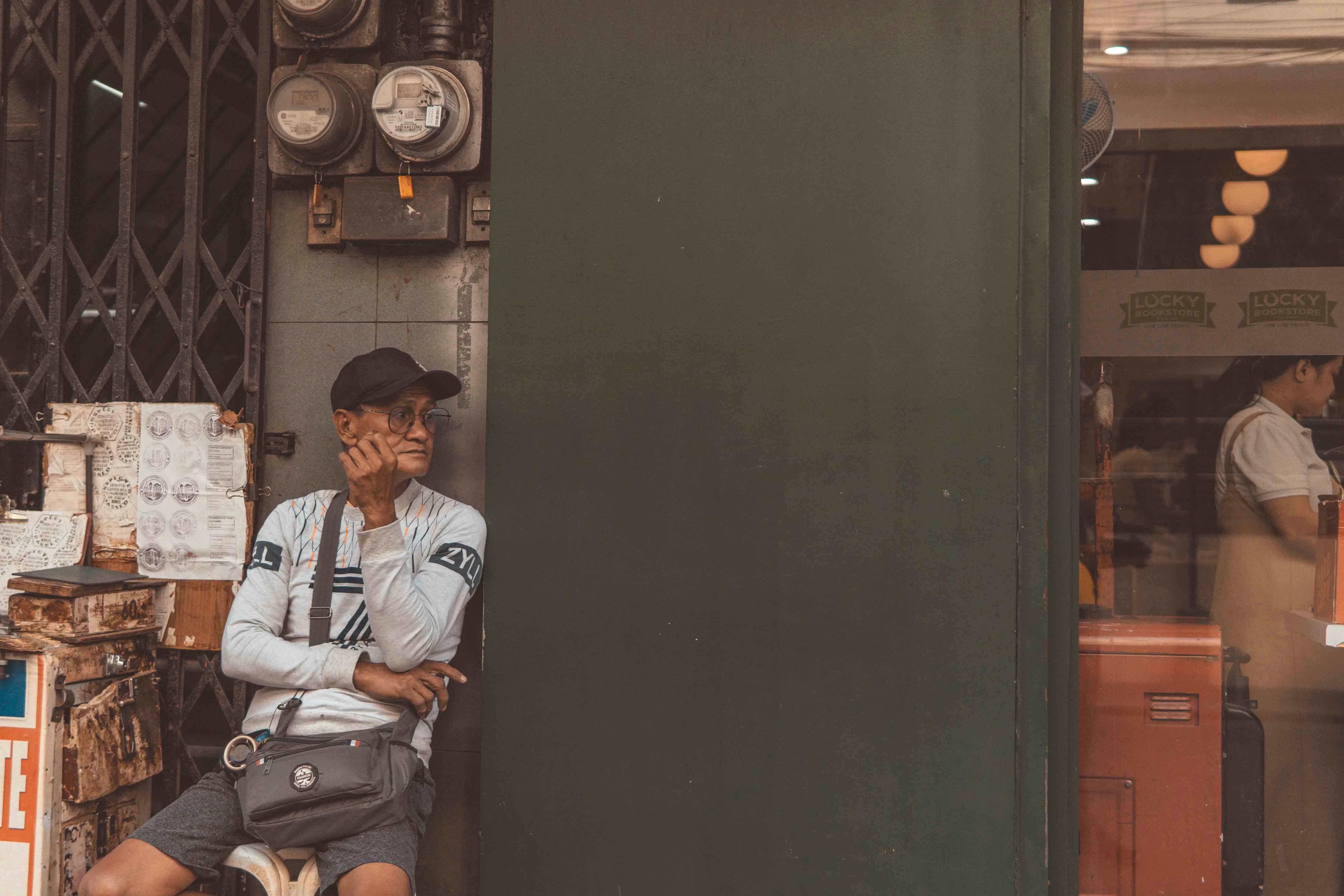 An urban scene with a man sitting outside a shop, reflecting deep in thought.