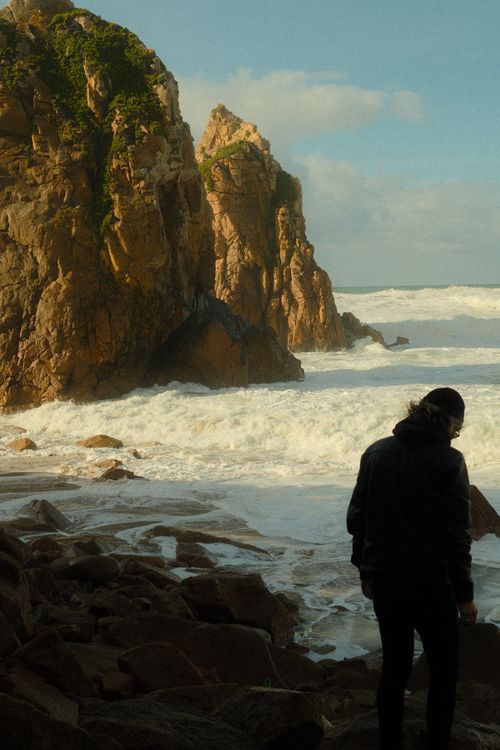 Free Dramatic view of Praia da Ursa with a person silhouetted against the rocky coastline and waves crashing. Stock Photo