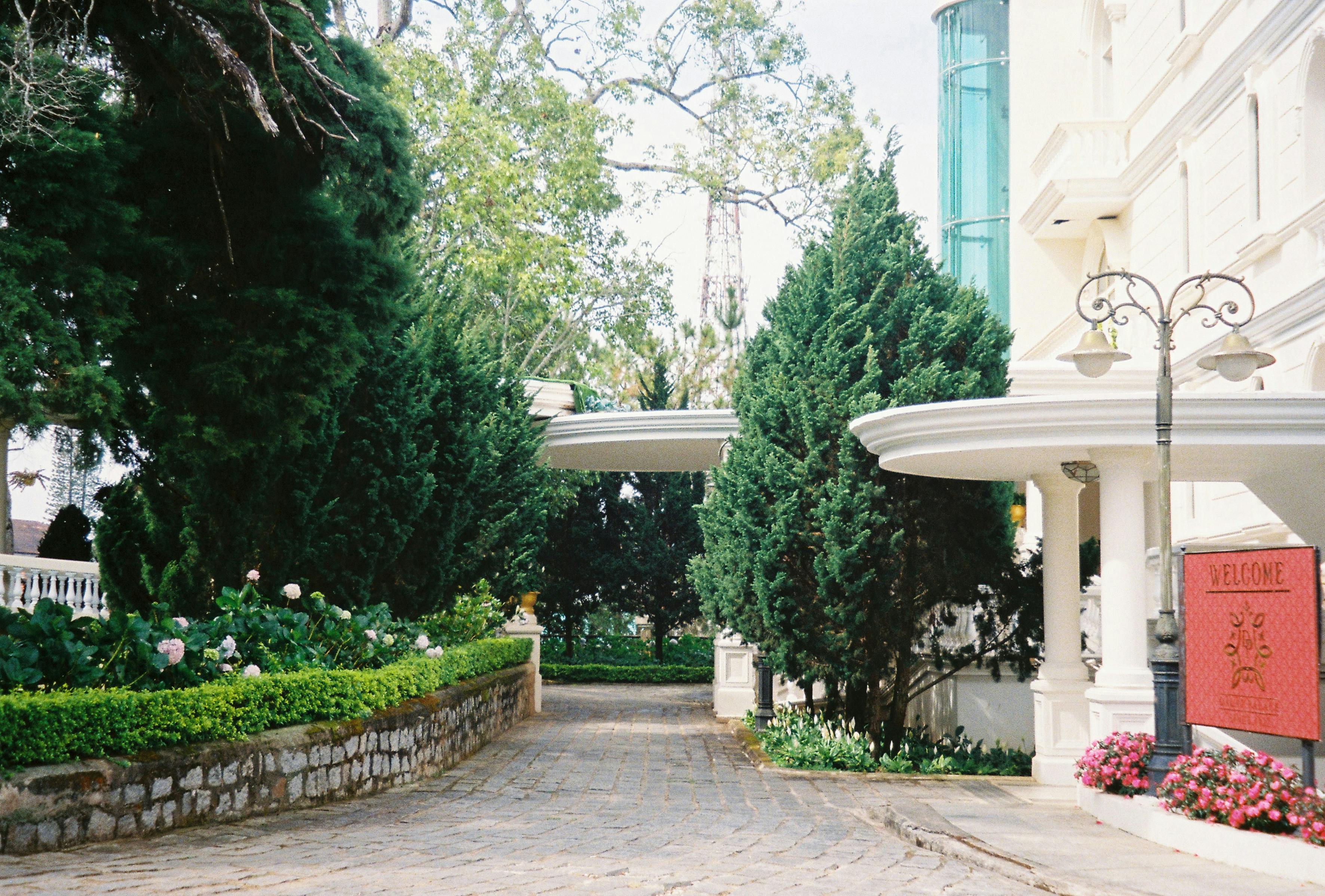Gratis Charmerende hotelindgang med grønne områder og velkomstskilt, perfekt til rejser og arkitekturtemaer. Lagerfoto