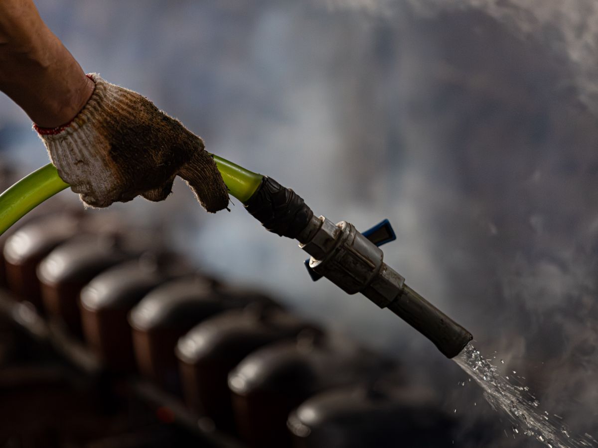 A gloved hand handling an industrial high pressure water hose with steam behind