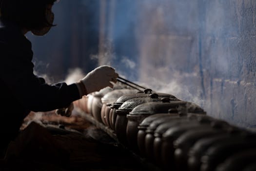 Person tending to steaming clay pots in a traditional Vietnamese kitchen, highlighting cultural cooking methods.