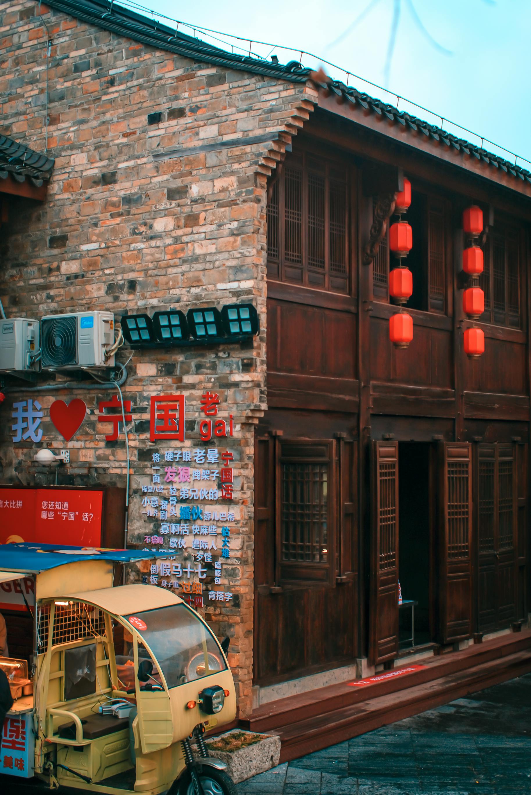 Gratuit Façade d'un bâtiment chinois traditionnel avec des lanternes rouges et un tuk-tuk jaune au premier plan. Photos