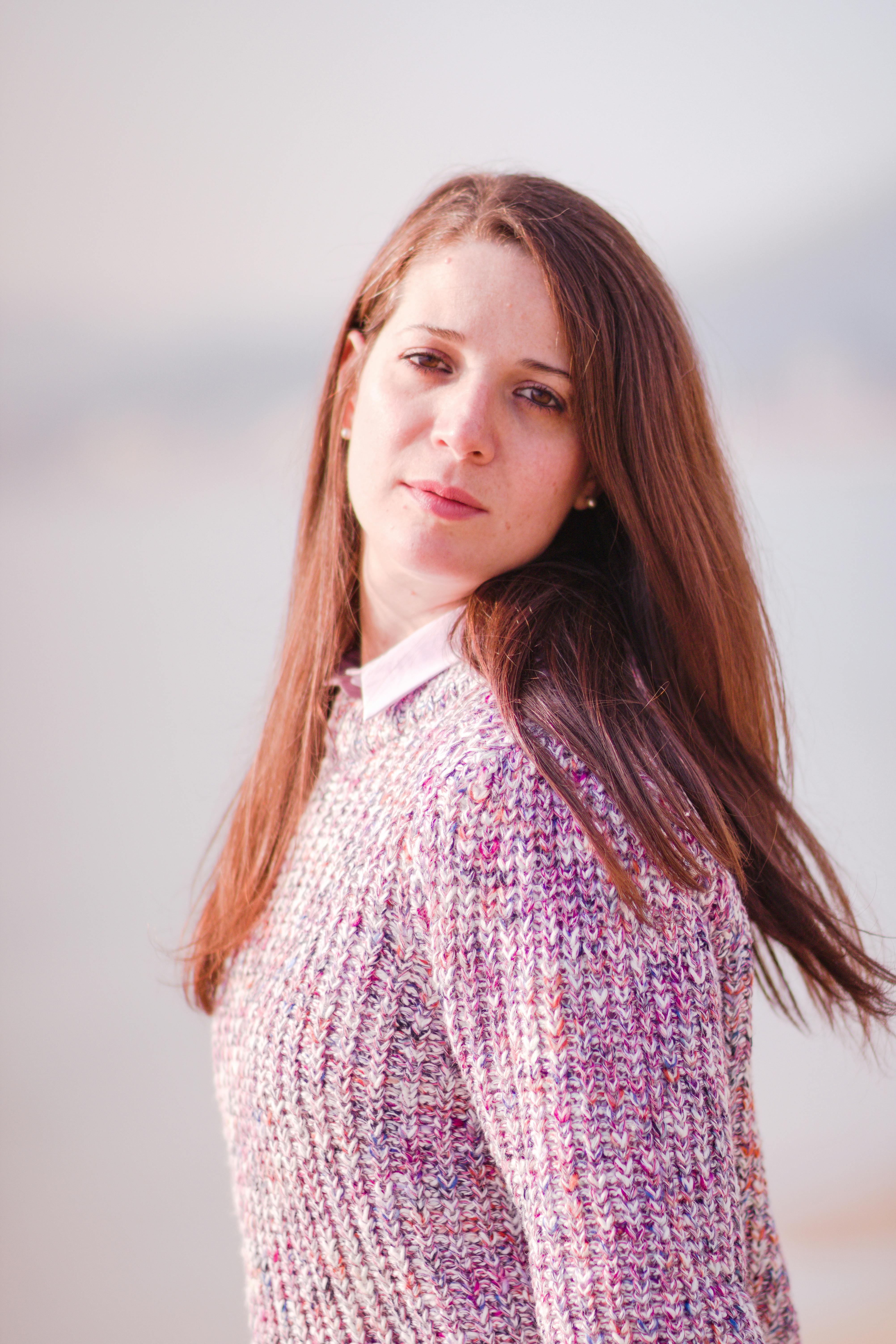 Gratis Affascinante ritratto di una donna con i capelli lunghi e un caldo maglione lavorato a maglia, all'aperto in un ambiente sereno. Foto a disposizione