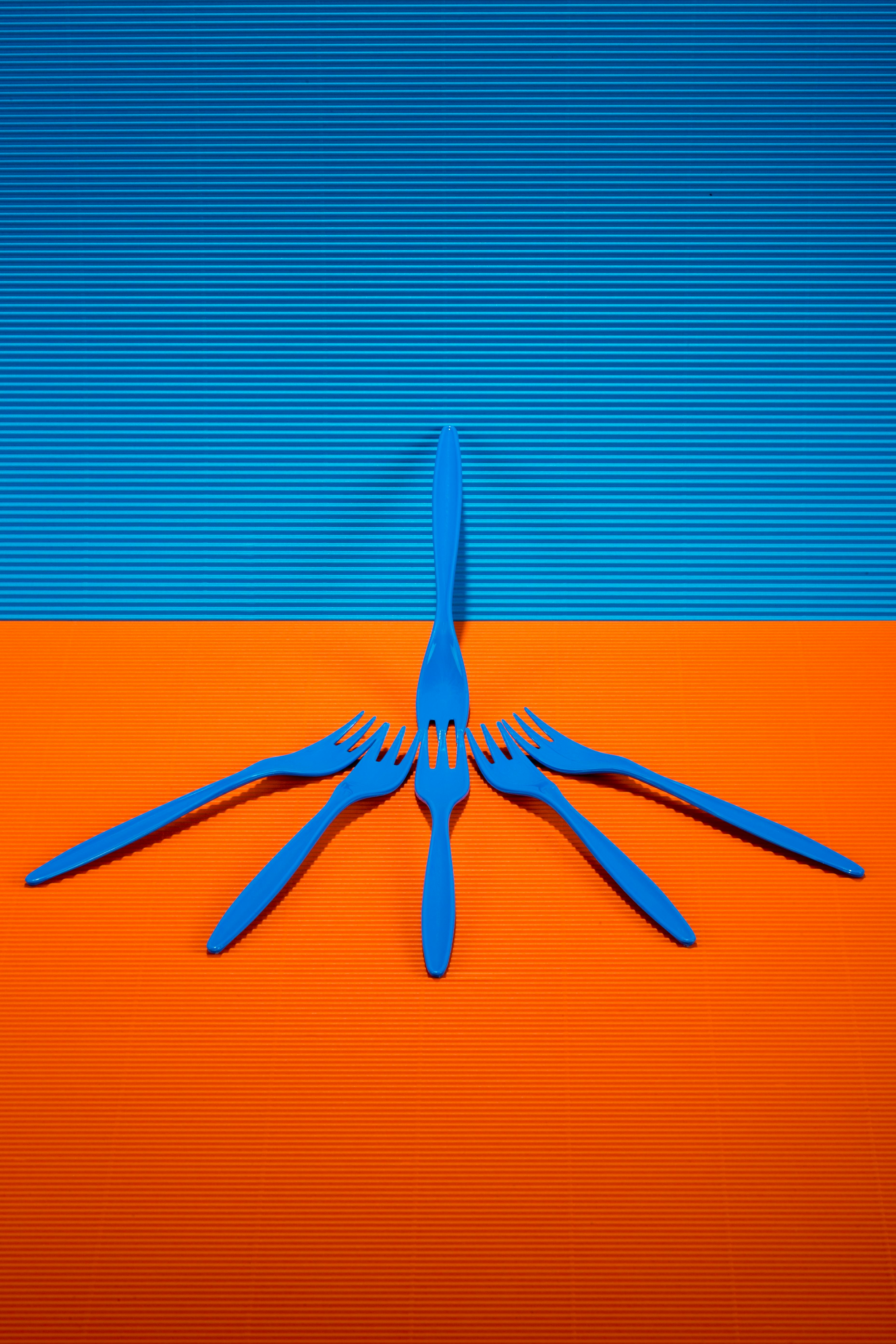 Free Artistic arrangement of blue forks on an orange surface with a blue backdrop creates a vivid contrast. Stock Photo