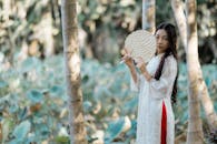 Woman in Traditional Dress Holding Fan in Forest