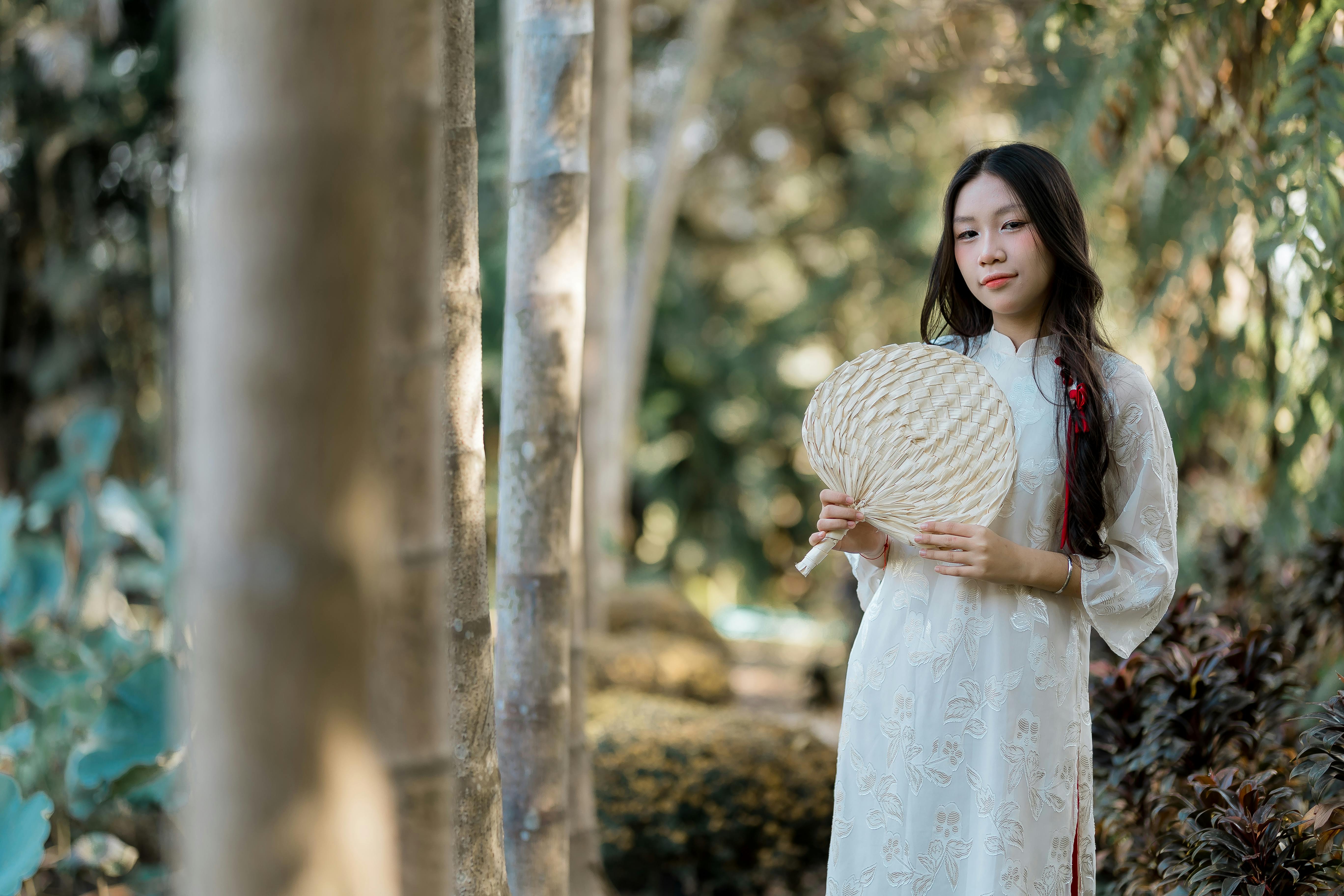 gratis Jonge vrouw in traditionele kleding met een waaier in haar hand te midden van een weelderige groene tuin, straalt rust en sereniteit uit. Stockfoto