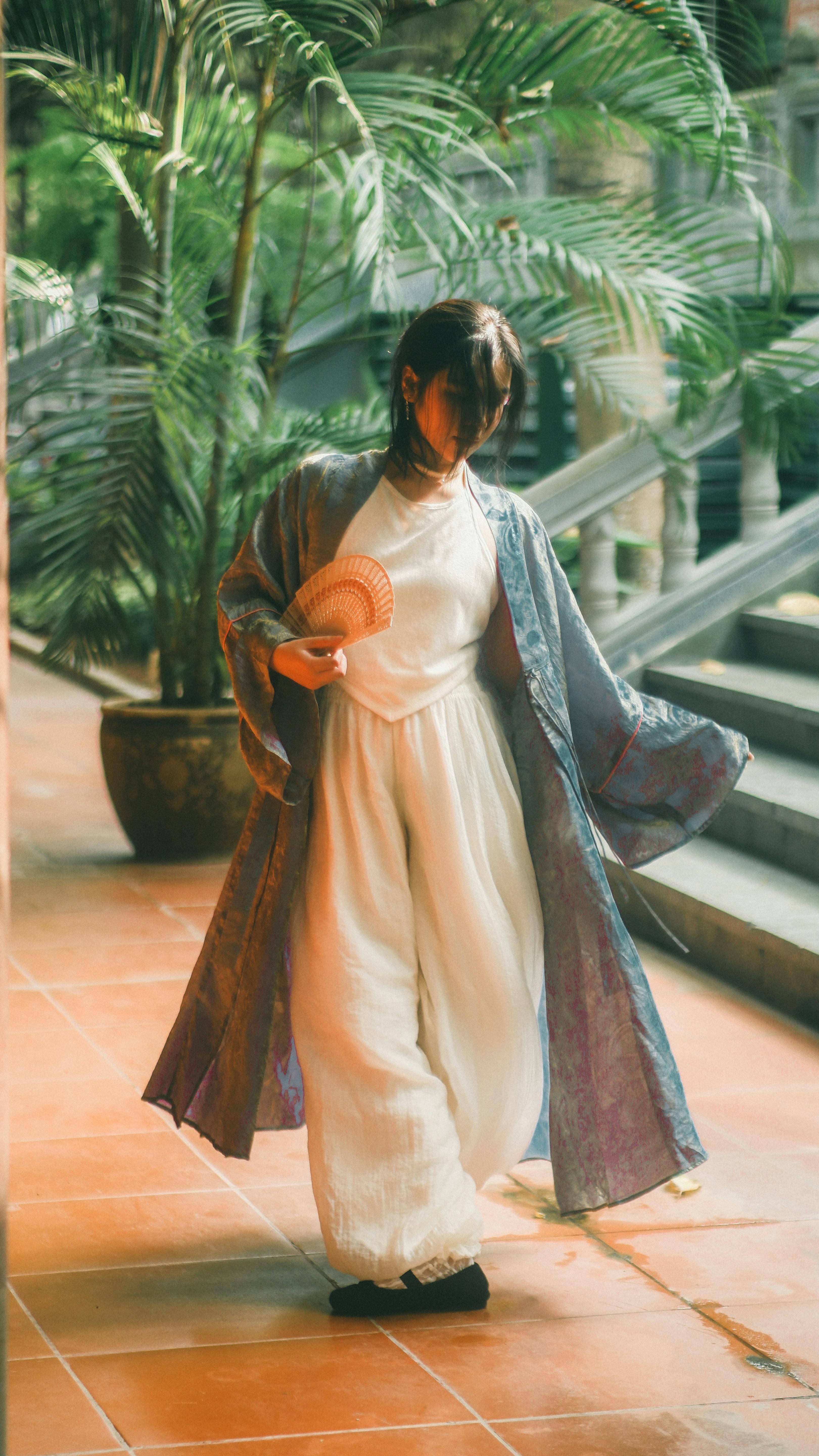 Free Serene moment of a woman in flowing attire holding a fan, exuding elegance. Stock Photo