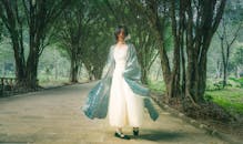 Woman in Light Dress Walking Through Forest Pathway