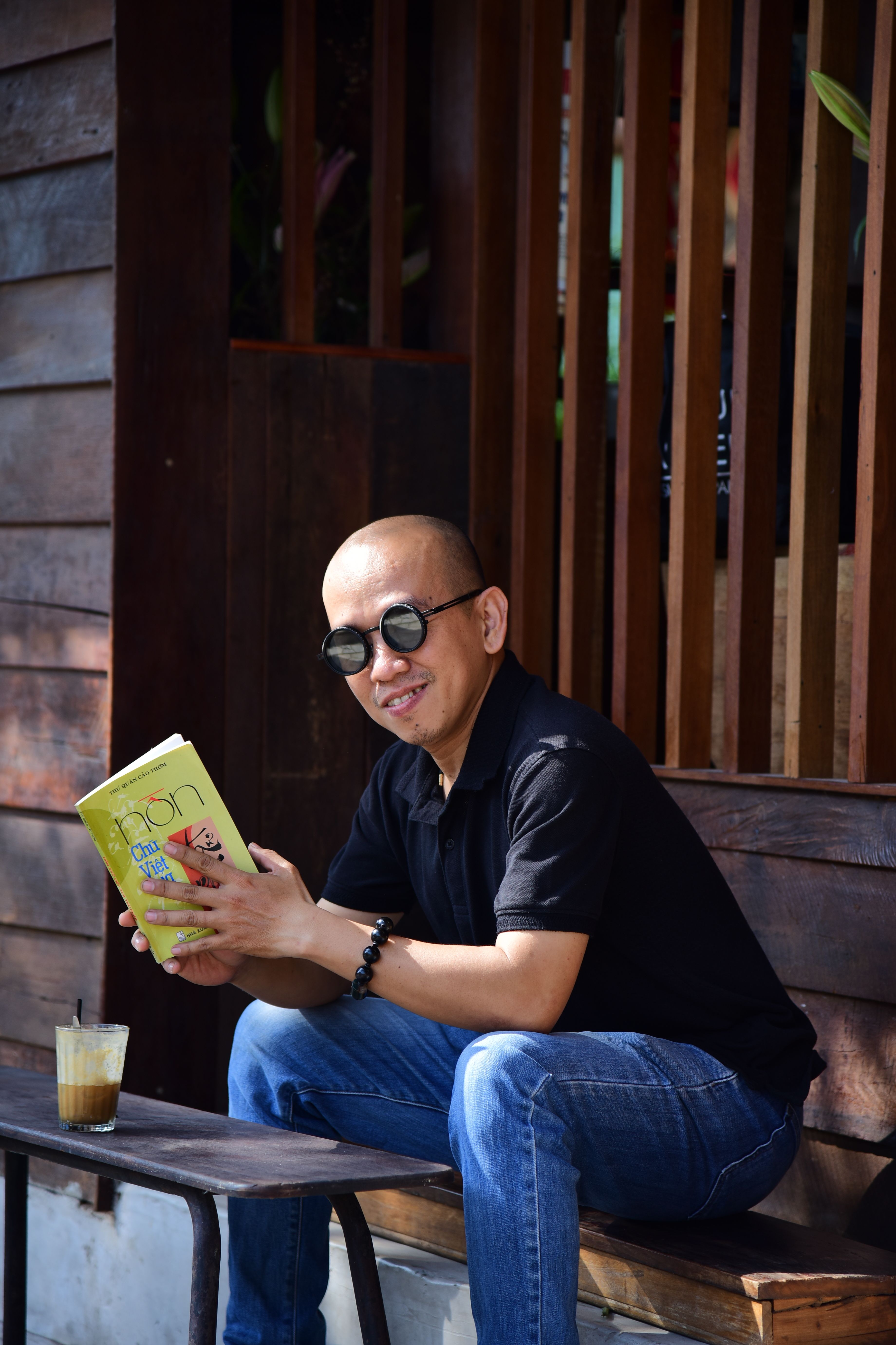 Man sitting outdoors reading a book with coffee on a sunny day, enjoying leisure time.