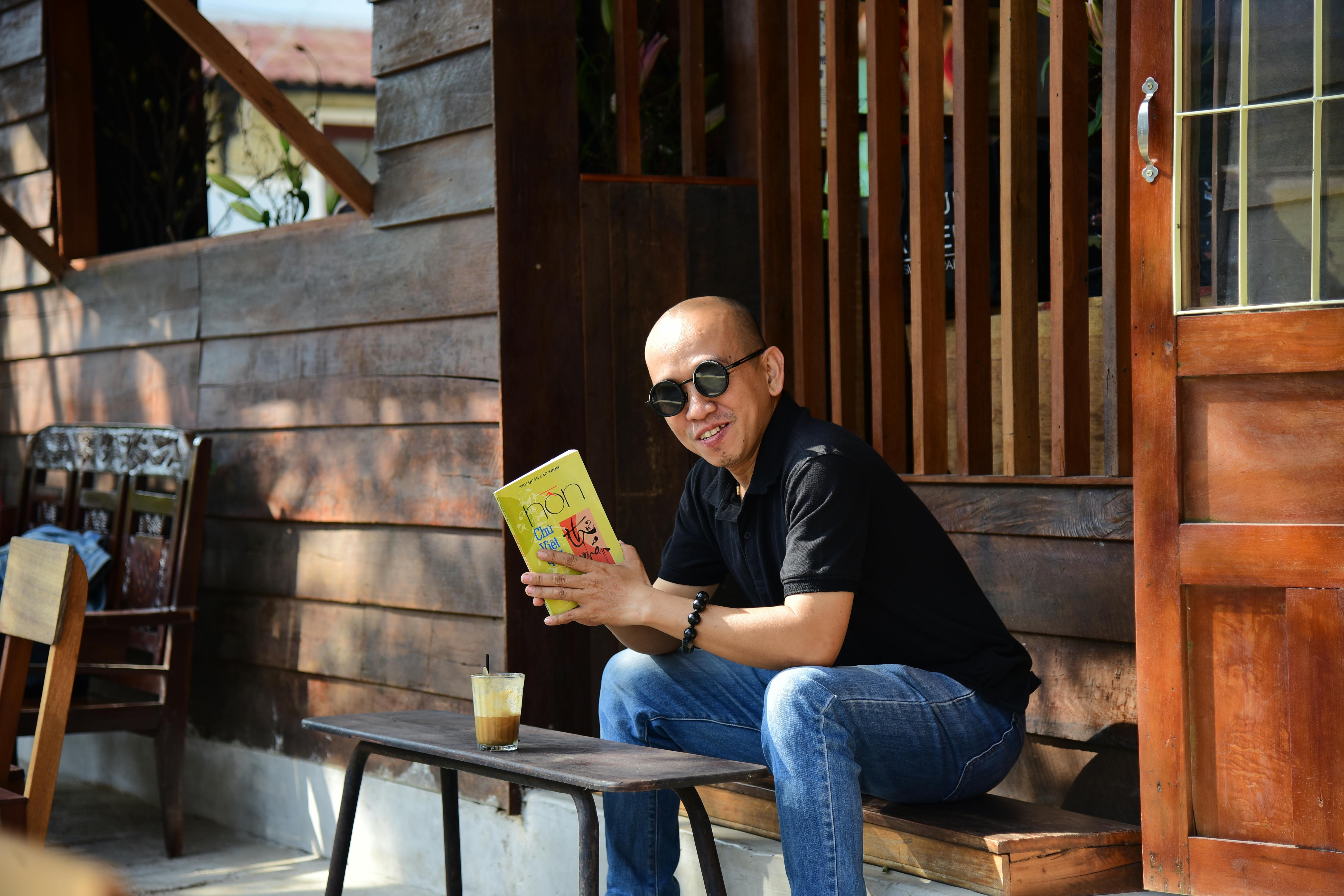 Man reading outdoors with iced coffee, enjoying a sunny day.