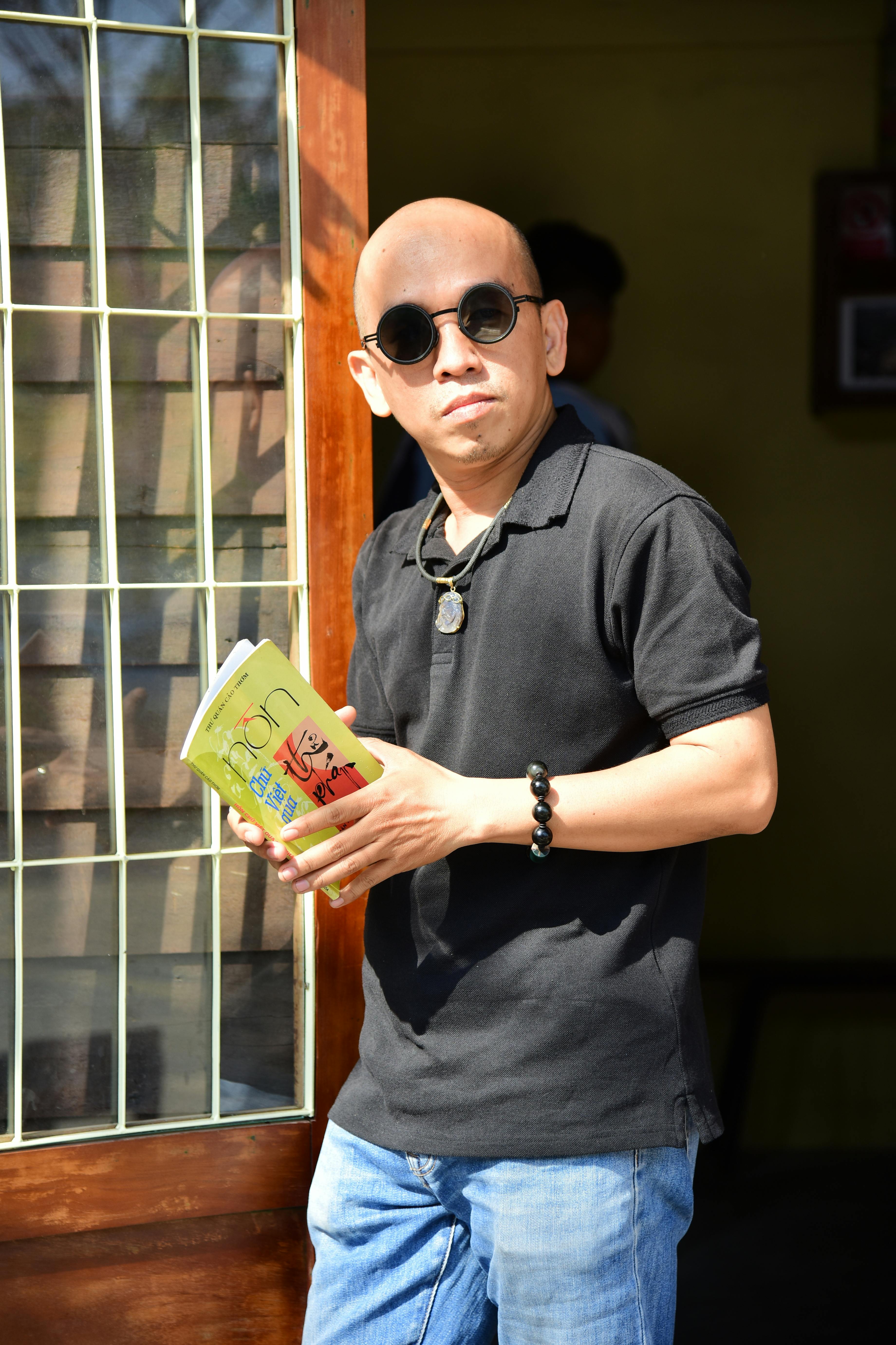 Δωρεάν Φαλακρός άντρας που φοράει γυαλιά ηλίου κρατώντας ένα βιβλίο και στέκεται έξω στο φως του ήλιου. Φωτογραφία από στοκ φωτογραφιών