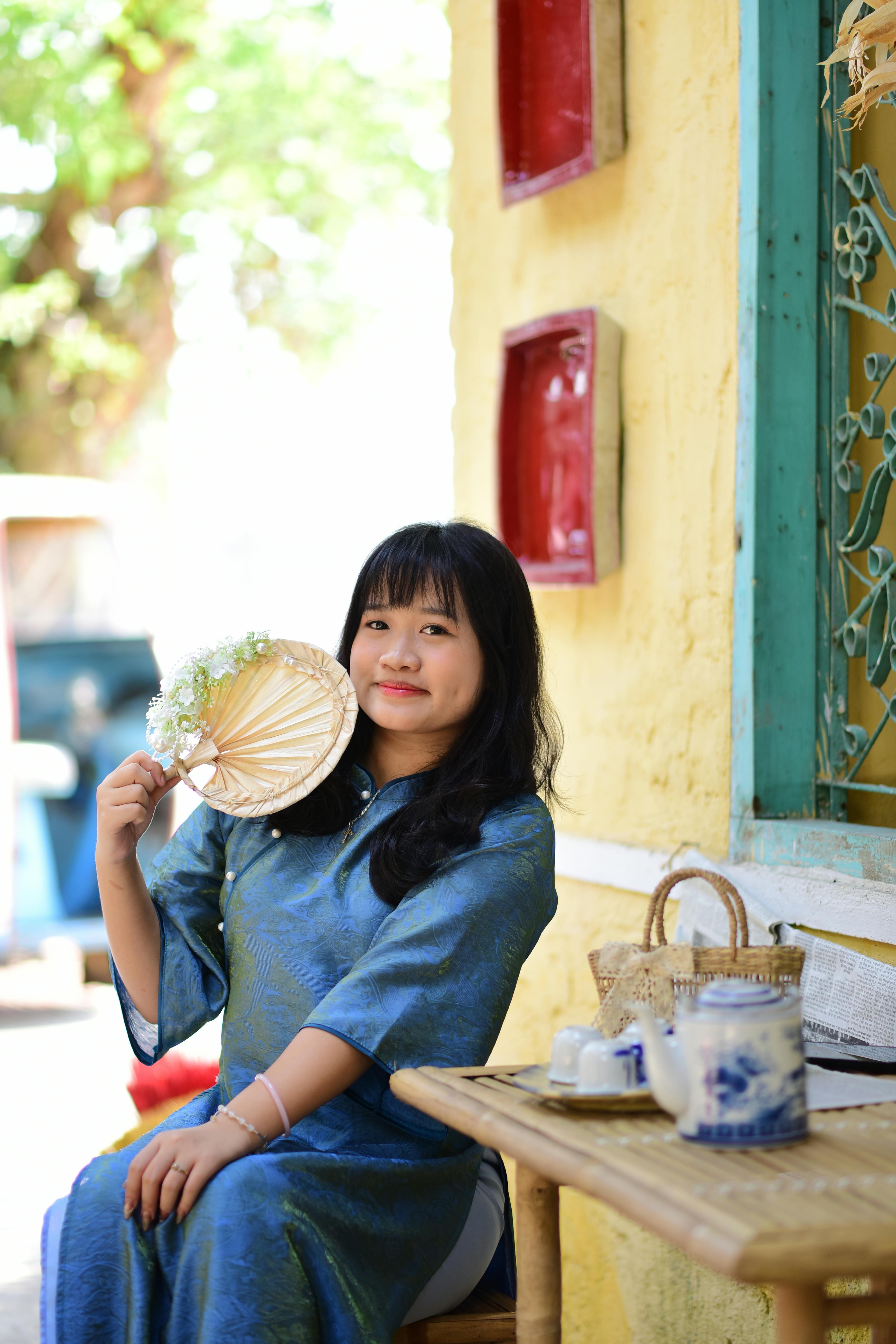 Ilmainen Perinteisessä asussa oleva aasialainen nainen pitelee viuhkaa istuessaan ulkona kahvilassa. Kuvapankkikuva