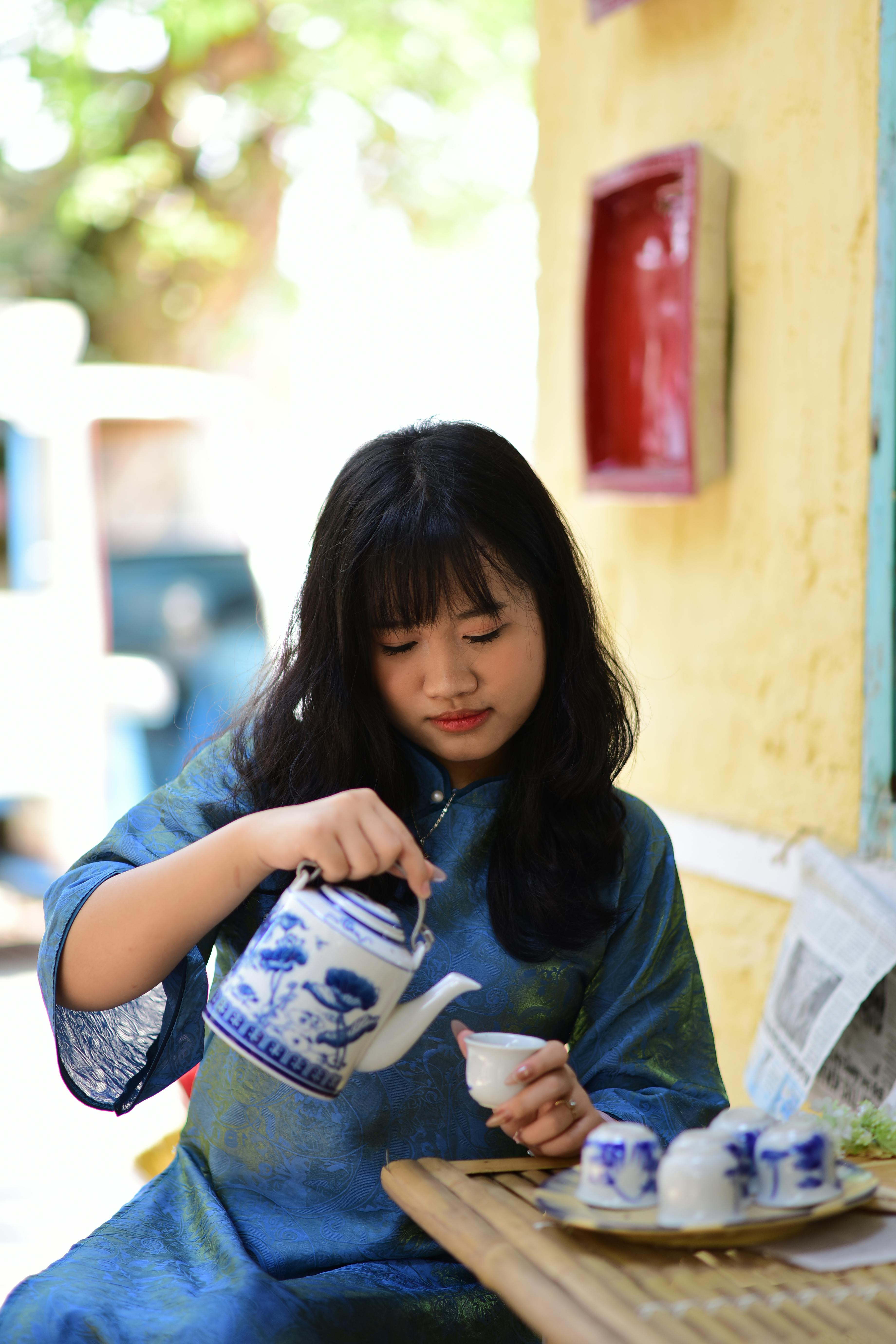 A young woman in traditional attire pours tea outdoors, embracing cultural heritage.