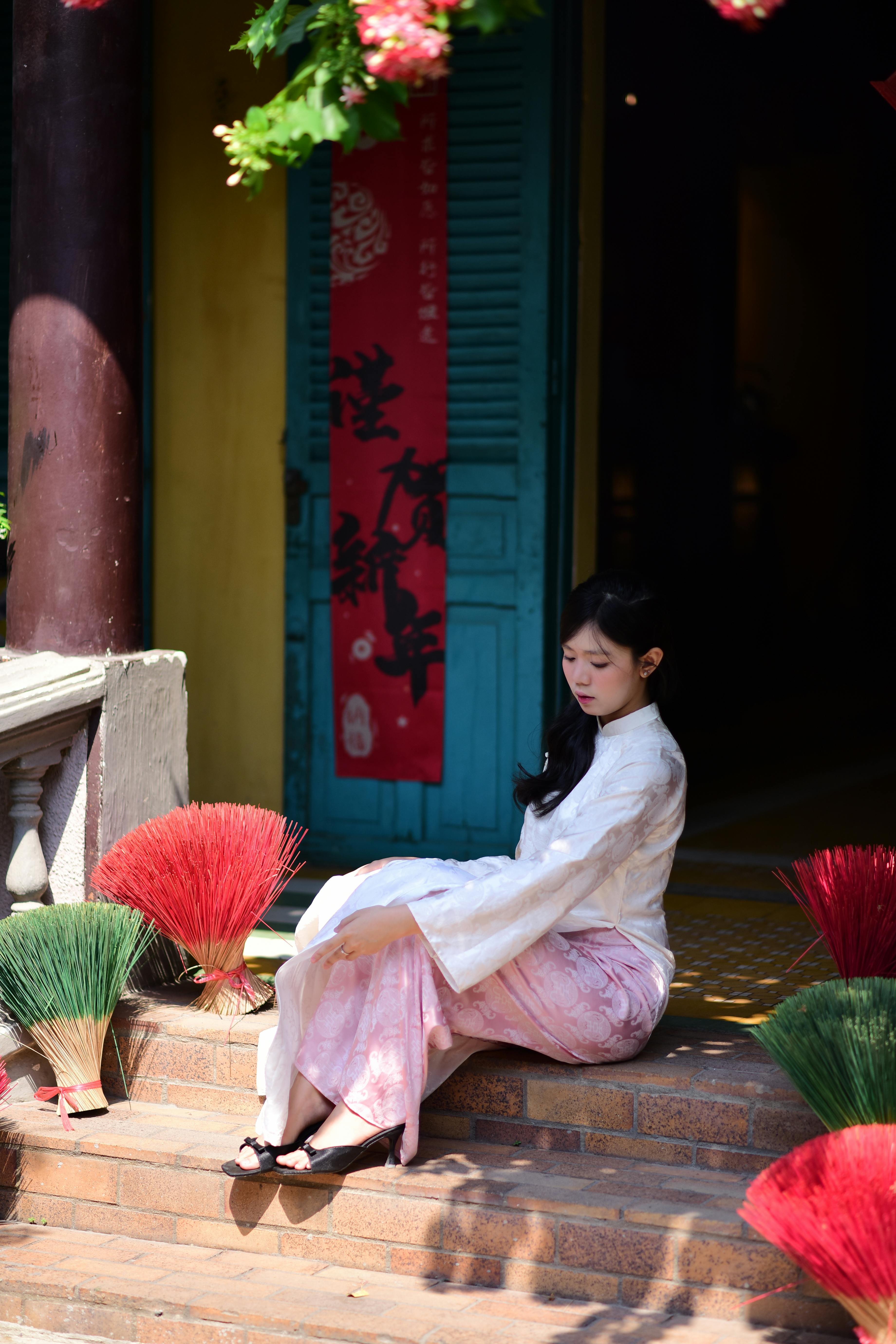 Ücretsiz Geleneksel kıyafetler giymiş genç bir kadının, rengarenk tütsü çubuklarının yanında oturduğu huzurlu bir sahne. Stok Fotoğraflar