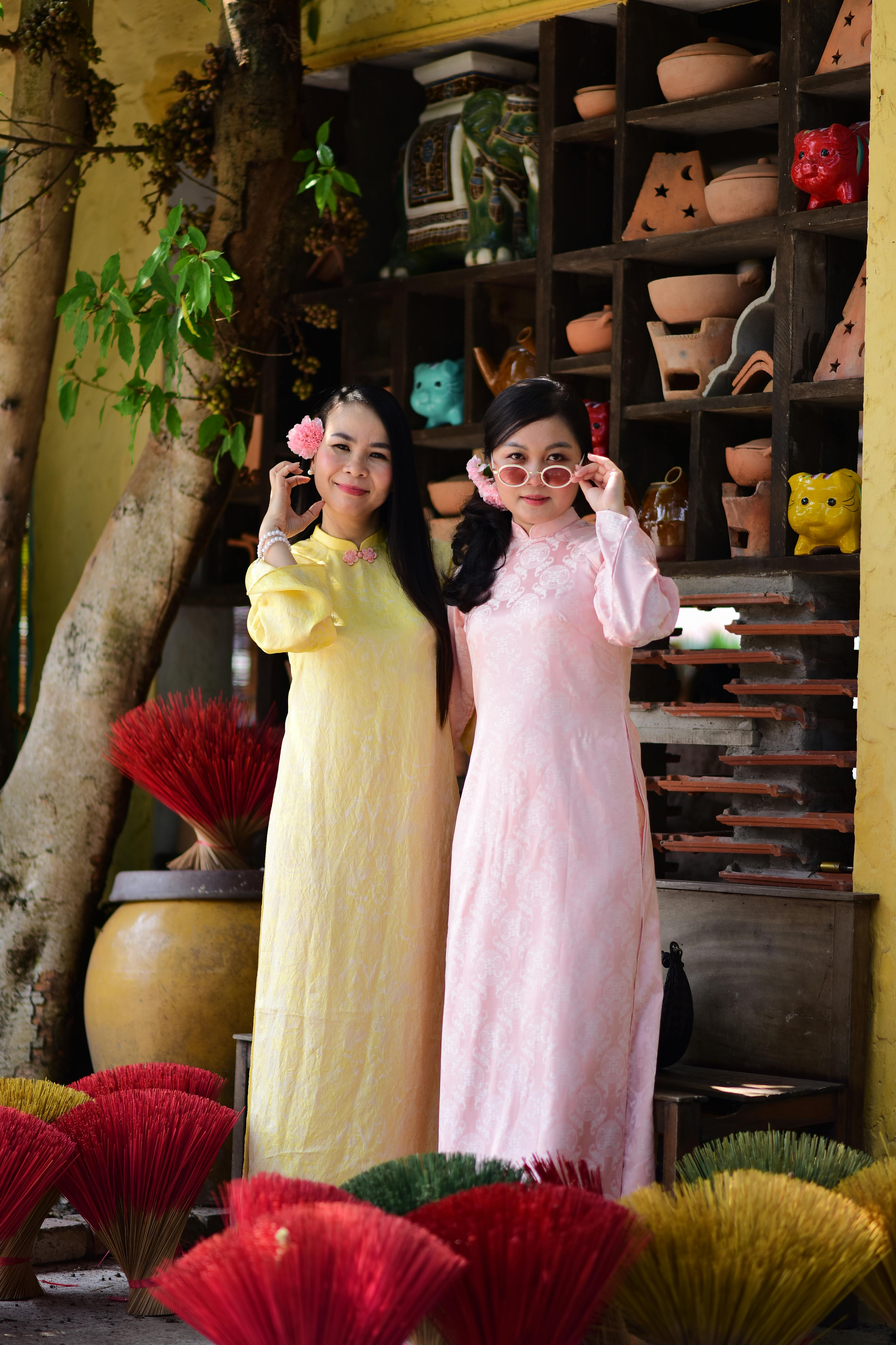 бесплатная Две женщины в традиционных нарядах позируют с благовонными палочками на фоне красочной обстановки. Азиатский декор. Стоковое фото