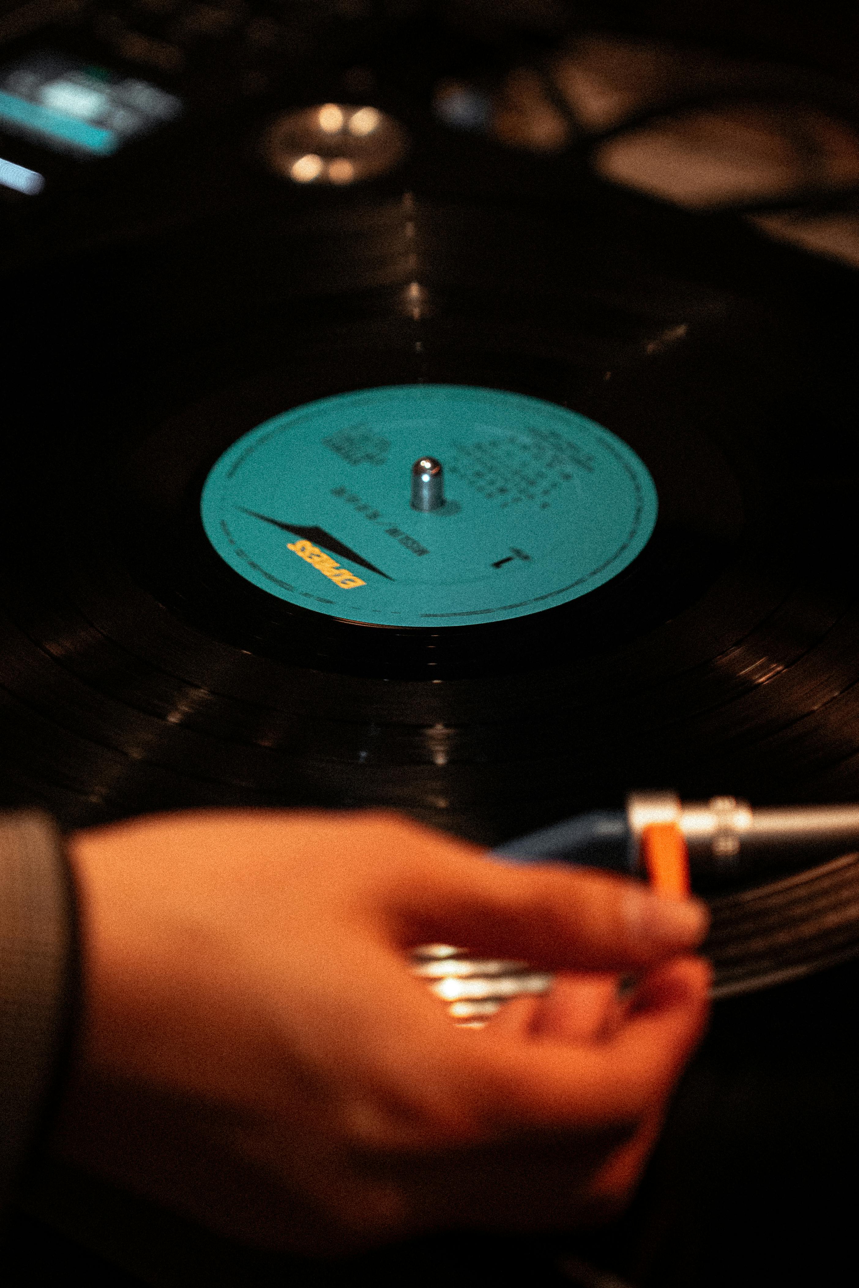 Ücretsiz Bir elin, pikap üzerindeki dönen vinil plağı ayarlaması ve plağın etiketine odaklanılması. Stok Fotoğraflar