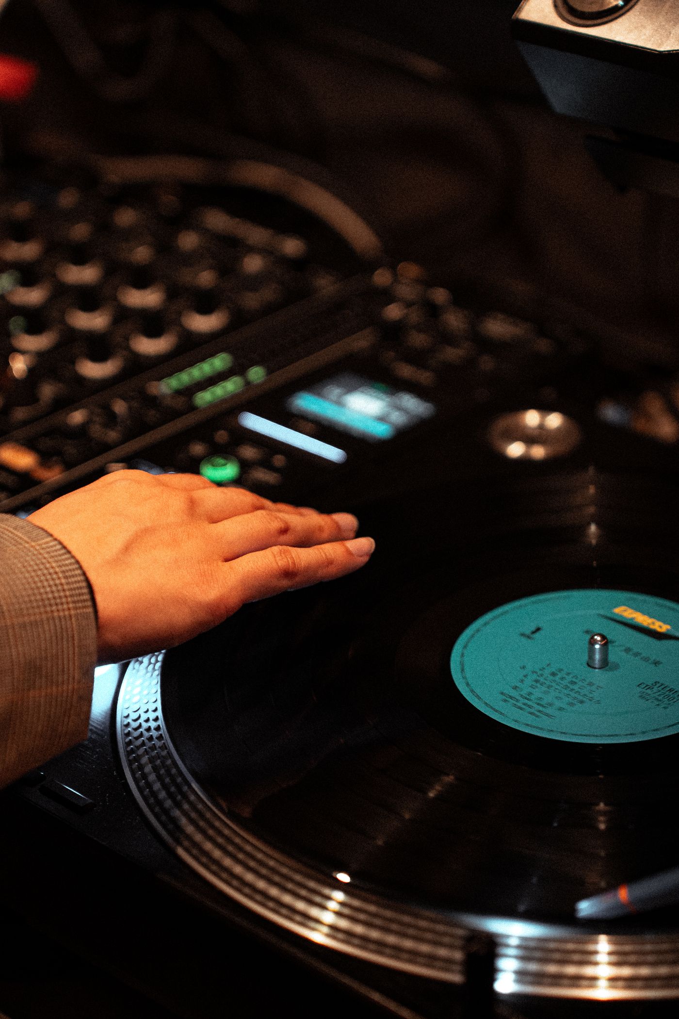 A DJ's hand spinning a vinyl record on a turntable in a dimly lit club