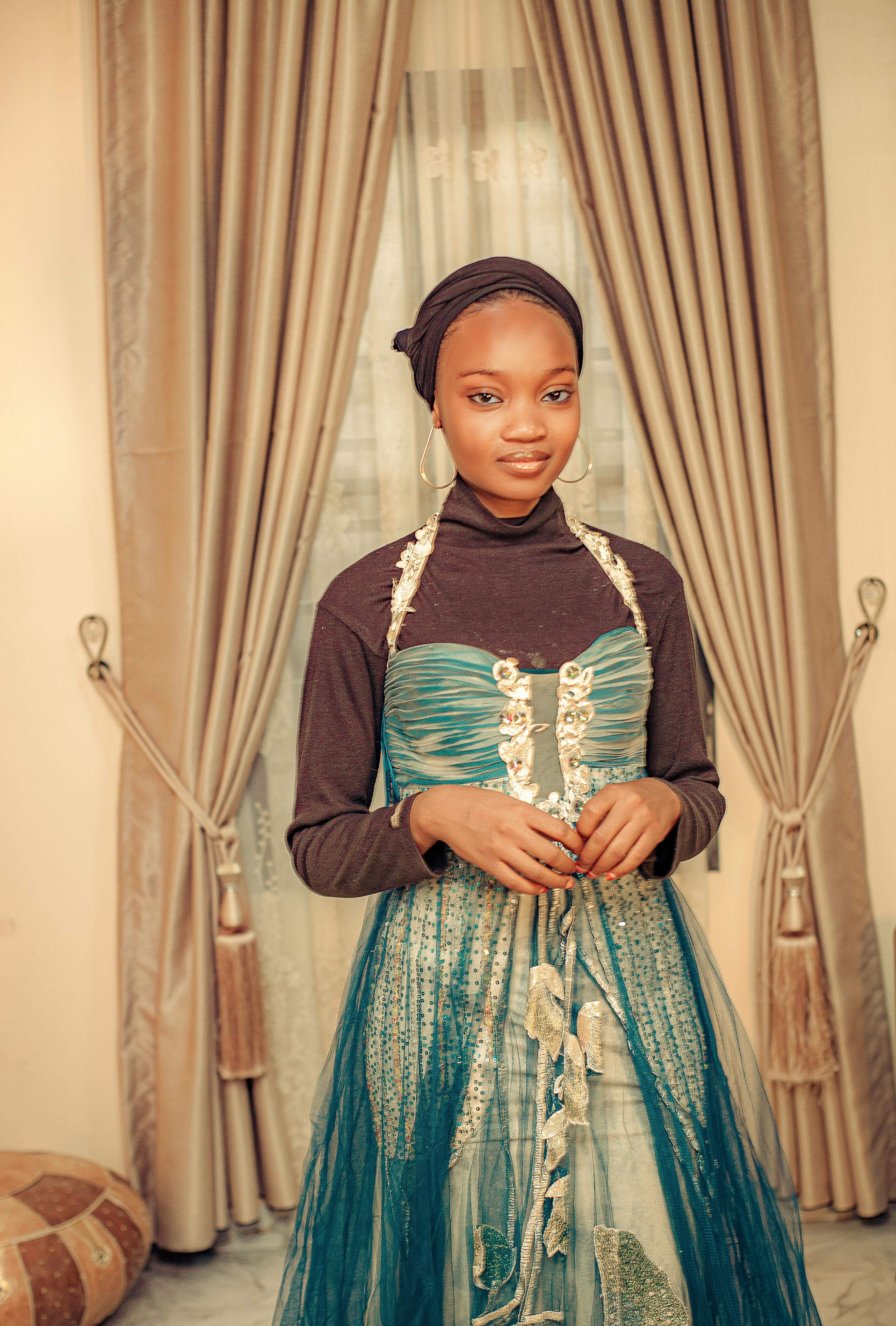 Miễn phí Một thiếu nữ duyên dáng trong chiếc váy xanh tạo dáng thanh lịch trong nhà với những tấm rèm sang trọng. Ảnh lưu trữ